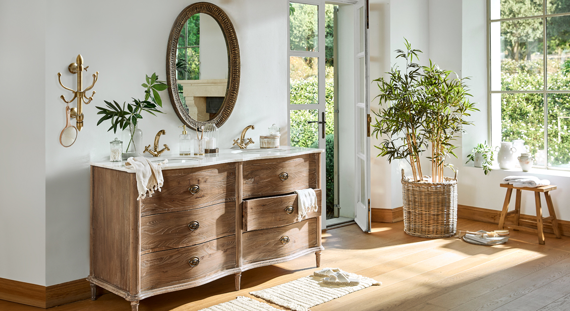 Holzkommode mit Marmorplatte und goldenen Armaturen in hellem Raum mit Pflanzen und Tageslicht