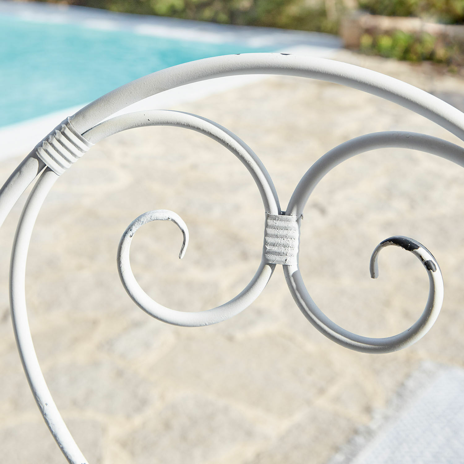 Weißes Metallornament eines Gartenmöbels mit geschwungenen Details vor Poolhintergrund