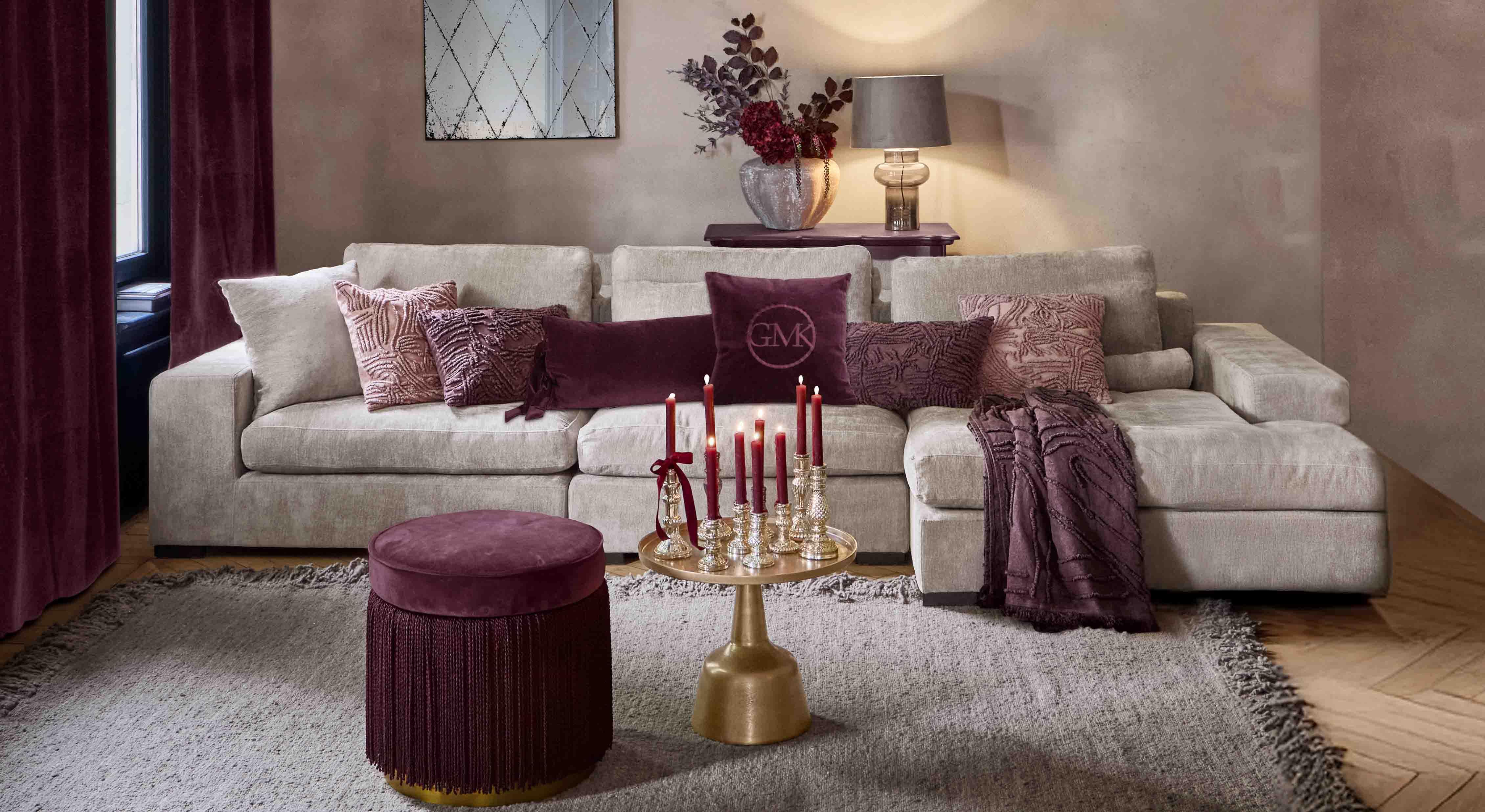 Beiges Sofa mit weichen Kissen und bordeauxfarbenen Akzenten in stilvollem Wohnzimmer mit Lampe und Spiegel