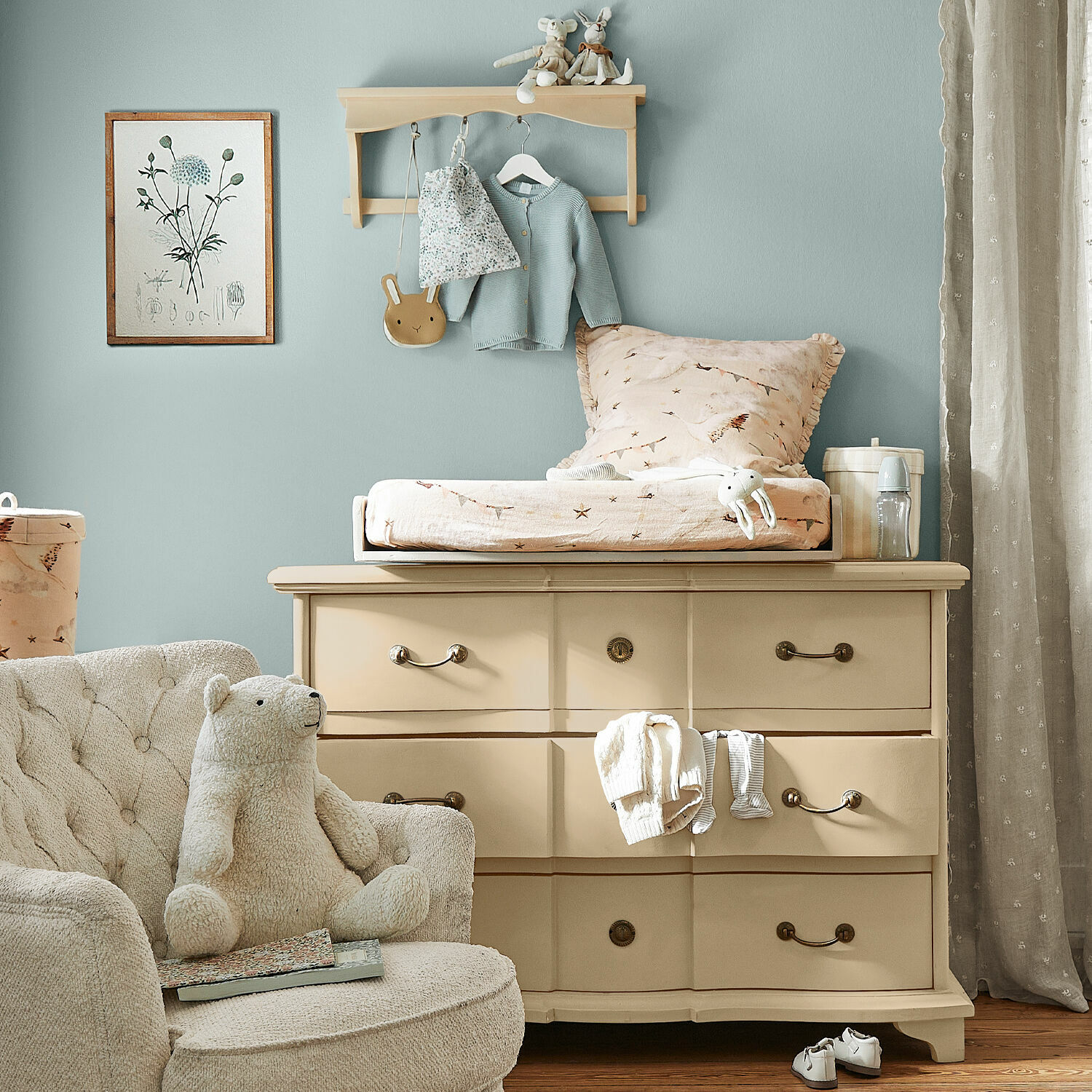Beige lackierte Holzkommode mit Wickelauflage und kuscheligem Sessel im Kinderzimmer