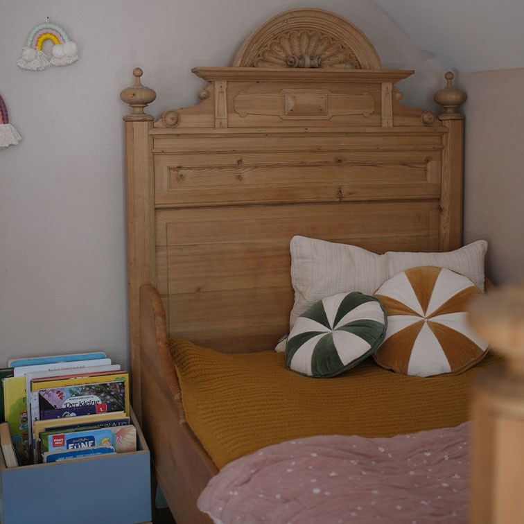 Massives Holzbett mit verziertem Kopfteil, dekorative Kissen und Bücher in einem Kinderzimmer
