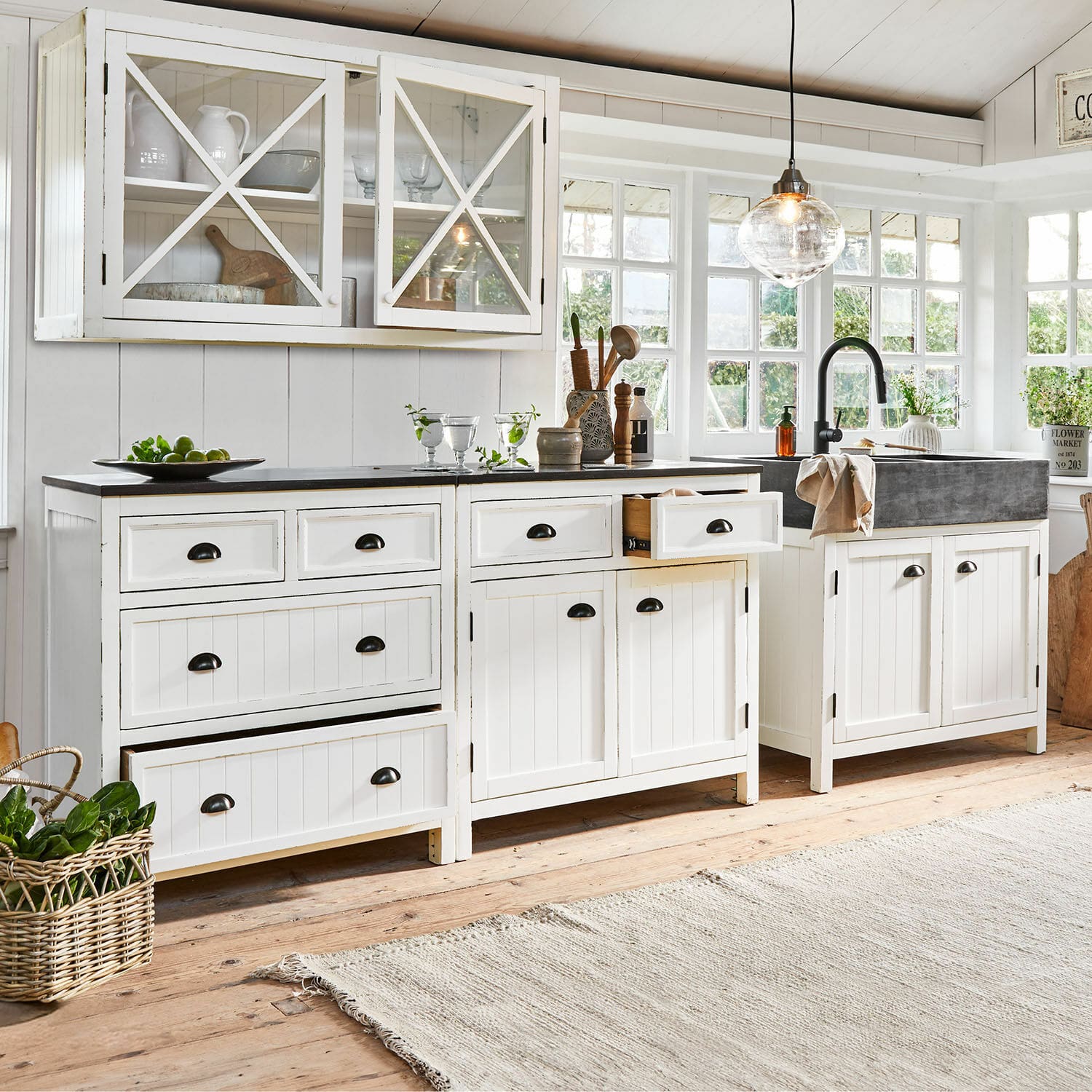 Weiße Holzküche mit schwarzer Arbeitsplatte und Spüle, helles Interieur mit großen Fenstern und Tageslicht