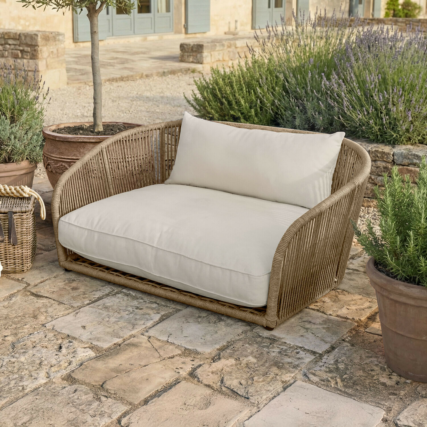 Outdoor-Sofa aus beigem Rattan mit cremefarbenen Kissen auf Steinboden neben Pflanzen
