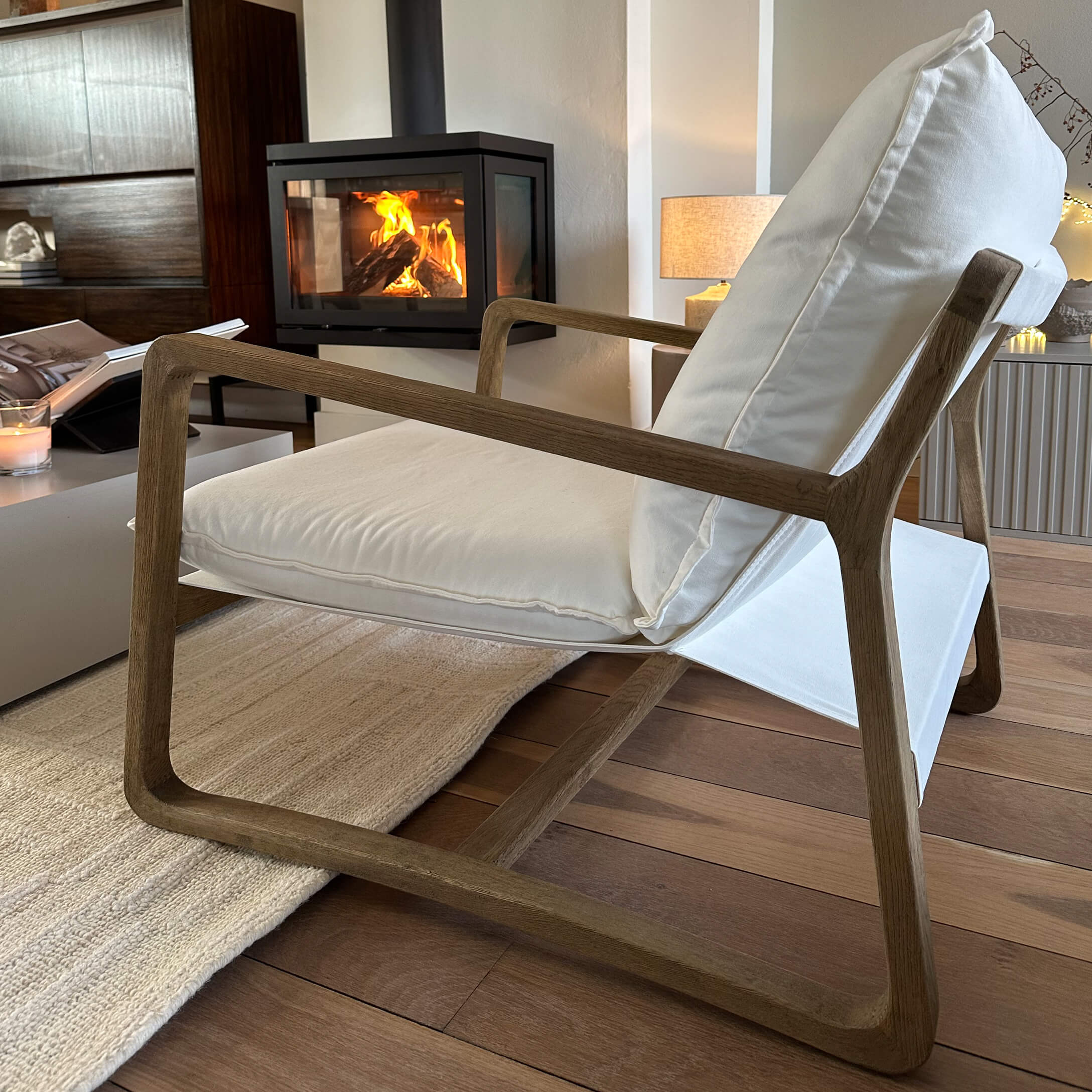 Moderner Sessel mit Holzrahmen und weißem Stoffbezug in gemütlichem Wohnzimmer mit Kaminfeuer