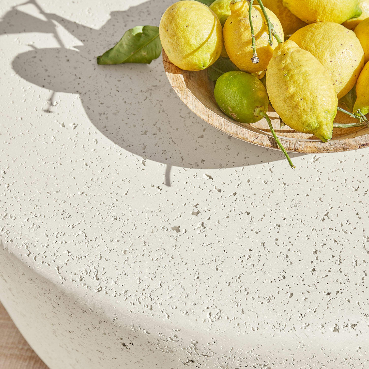 Runder weißer Tisch mit strukturierter Oberfläche und Schale mit gelben Zitronen auf Terrasse