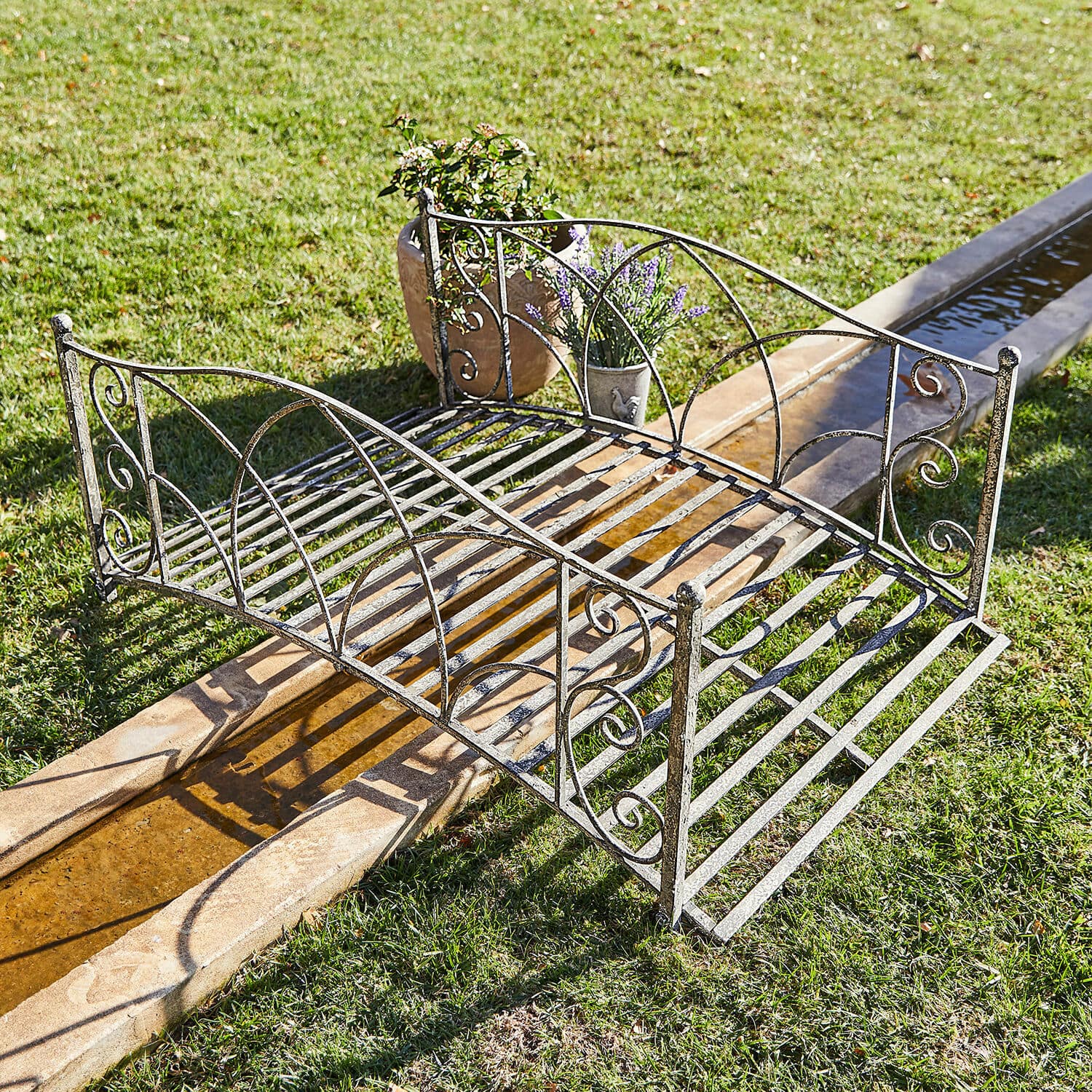 Deko-Brücke Escàs Elegante Metall-Gartenbrücke in antik-silberner Optik über Wasserlauf auf grünem Rasen