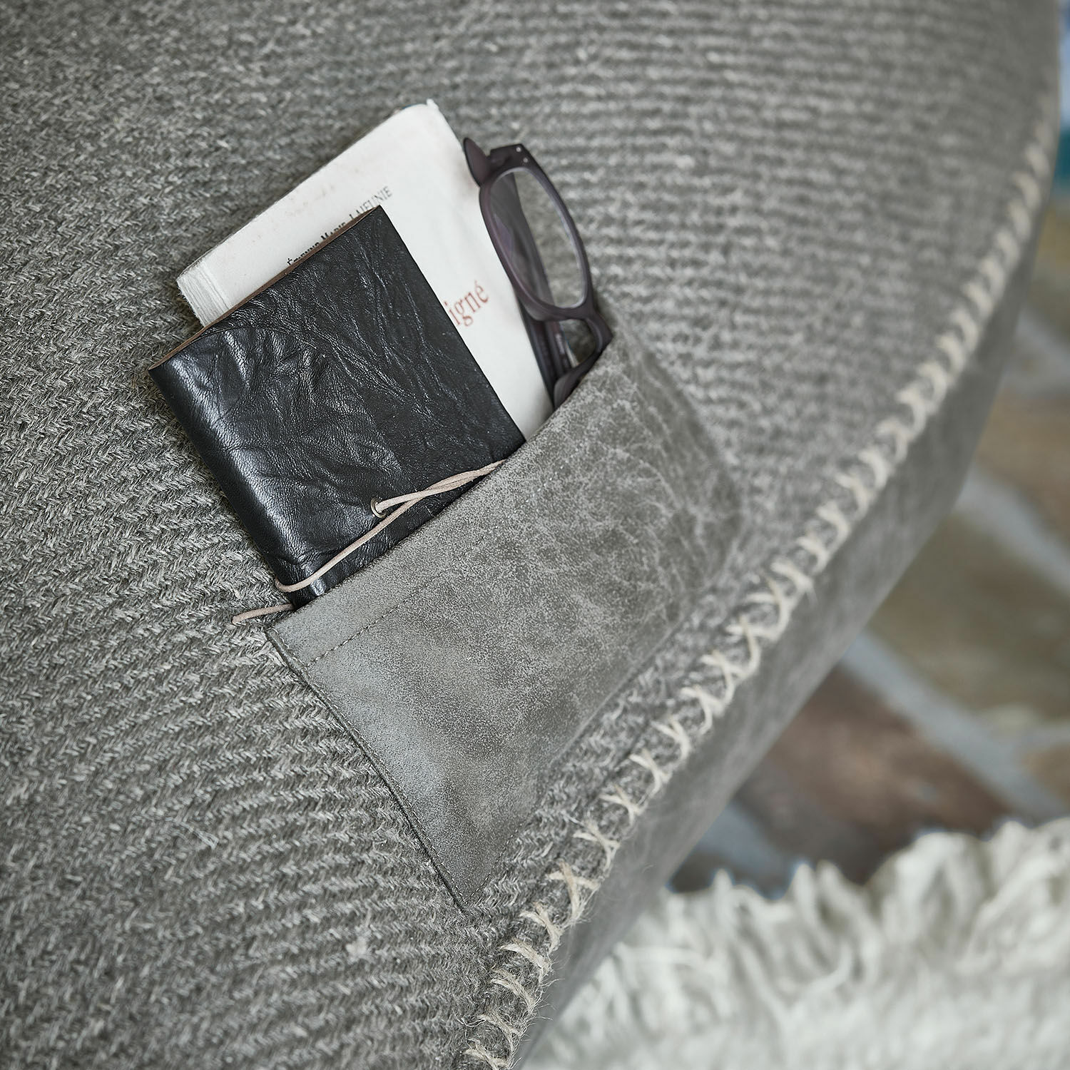 Grauer Stoff mit Wildledertasche, schwarzes Leder-Notizbuch und Lesebrille stecken darin