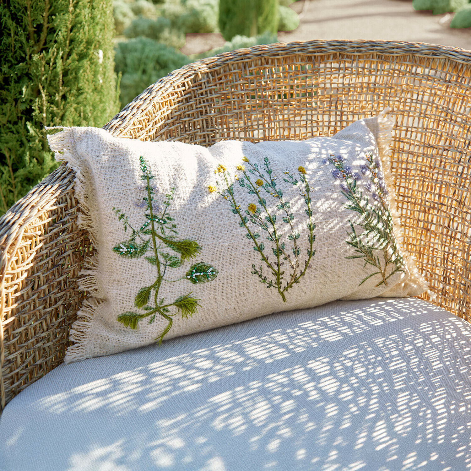 Beiges Leinenkissen mit Pflanzenstickerei auf Rattansessel, Gartendekoration