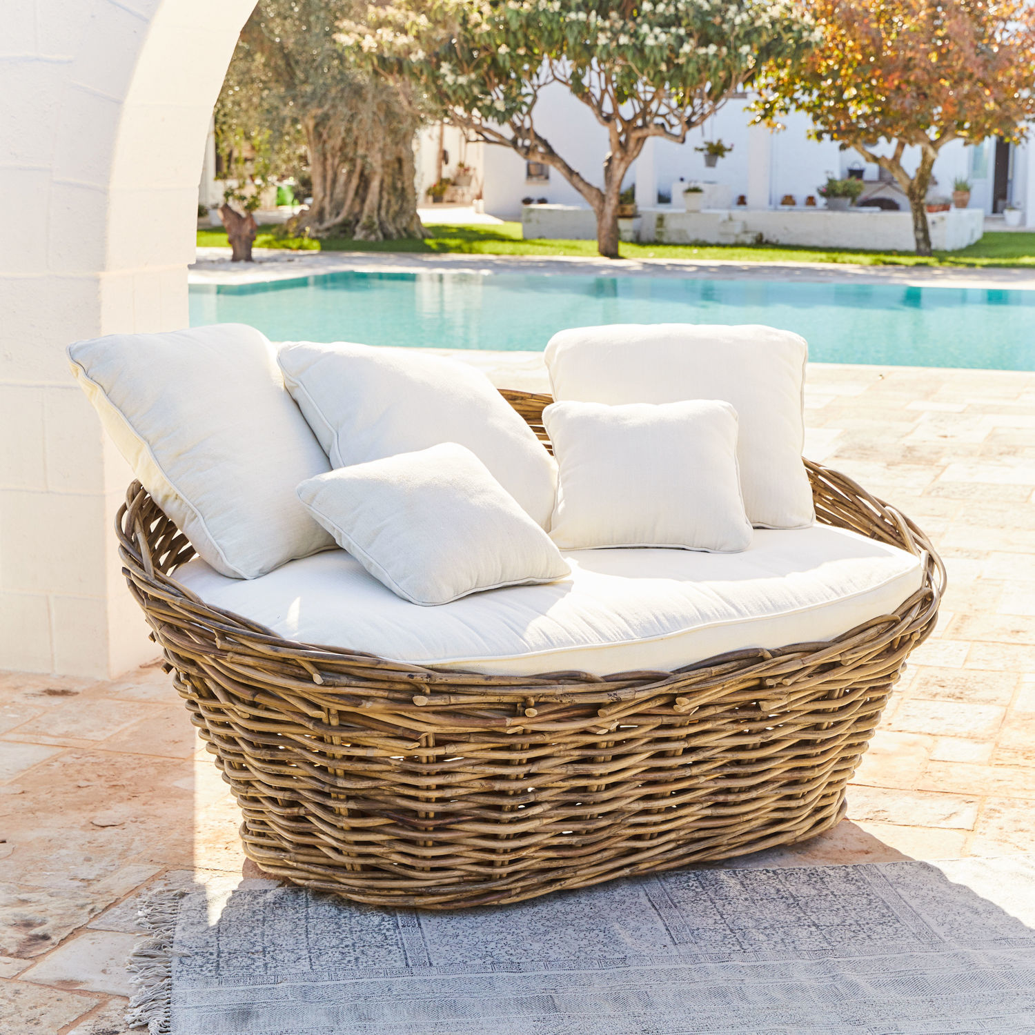 Runder Rattansessel mit weißen Kissen auf Terrasse am Pool, Gartenmöbel für draußen