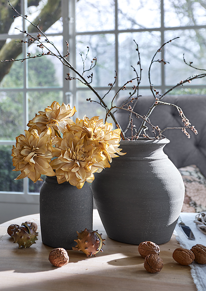 Zwei graue Keramikvasen mit getrockneten Blumen und Zweigen auf Holztisch mit Nüssen