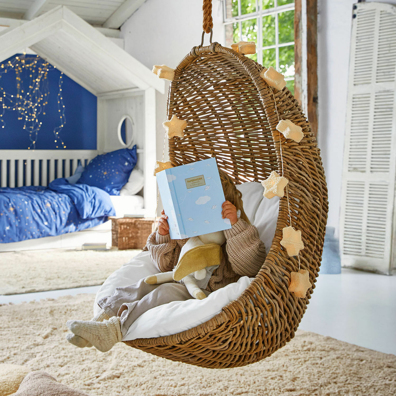 Hängesessel aus natürlichem Rattan mit weißem Kissen und Sternlichterkette im Kinderzimmer