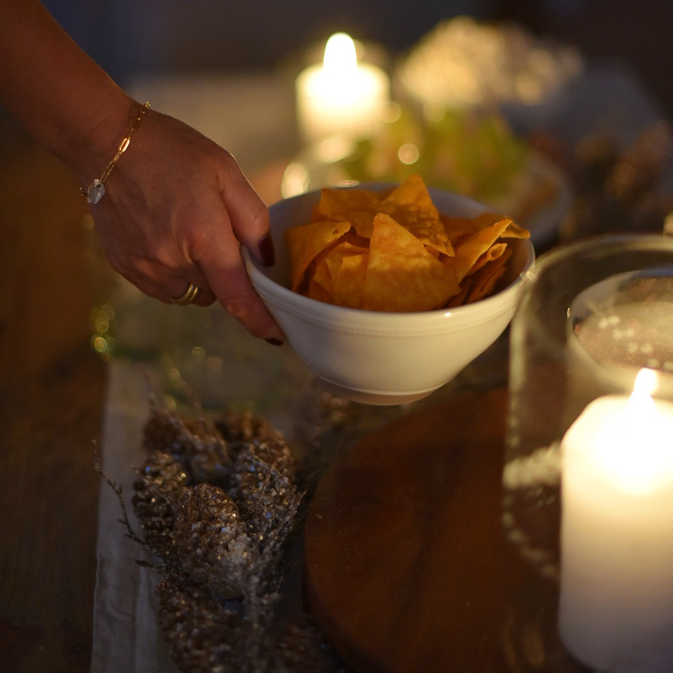 Hand hält weiße Schüssel mit orangen Chips vor Kerzenlicht und festlicher Dekoration