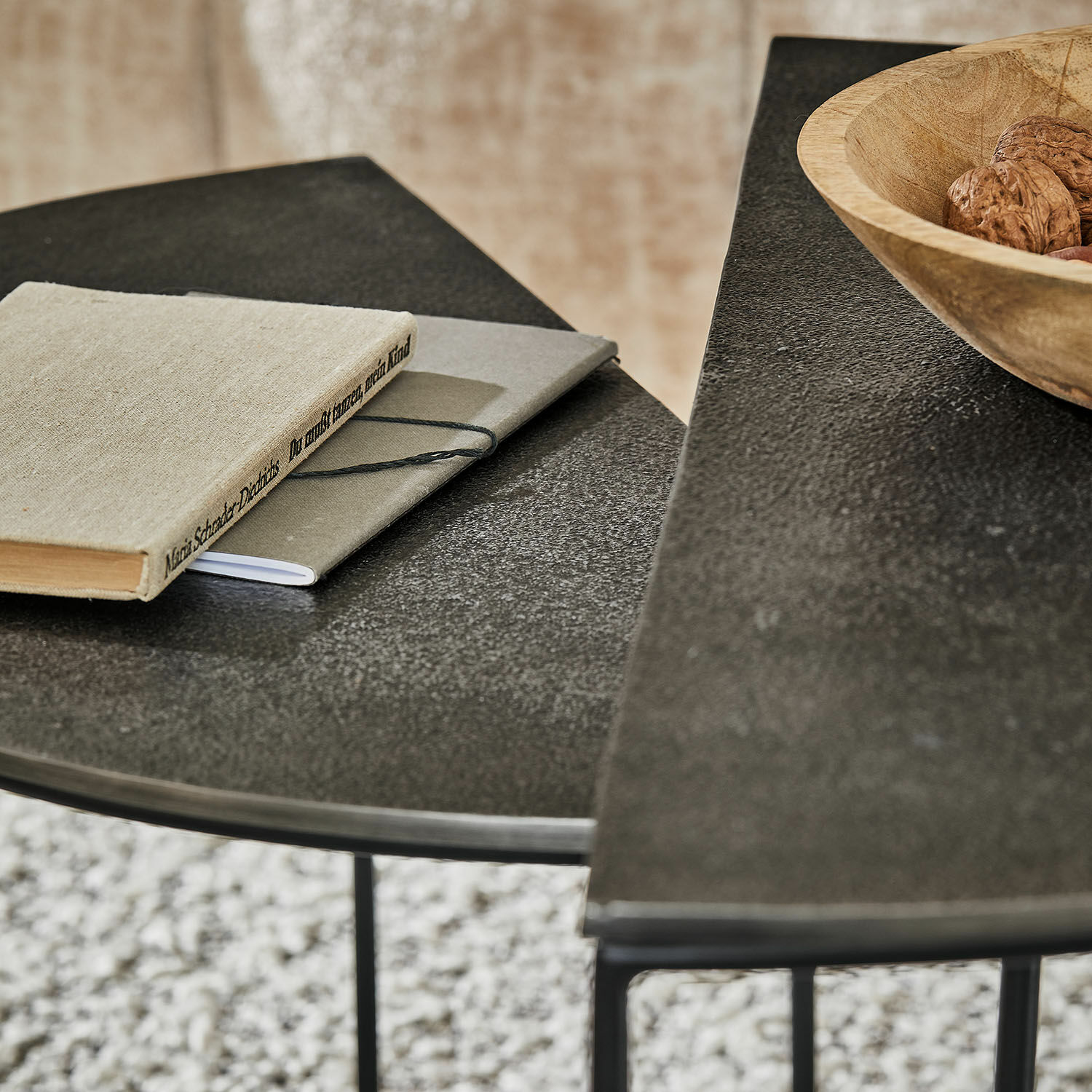 Schwarze Metalltische mit strukturierter Oberfläche, darauf Holzschale mit Nüssen und zwei graue Notizbücher
