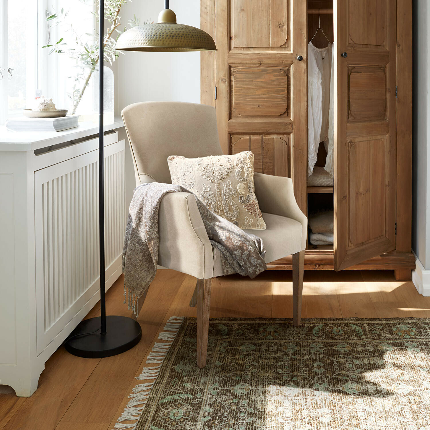 Beiger Sessel mit Holzbeinen, dekorativem Kissen und Decke in gemütlichem Wohnzimmer mit Holzschrank