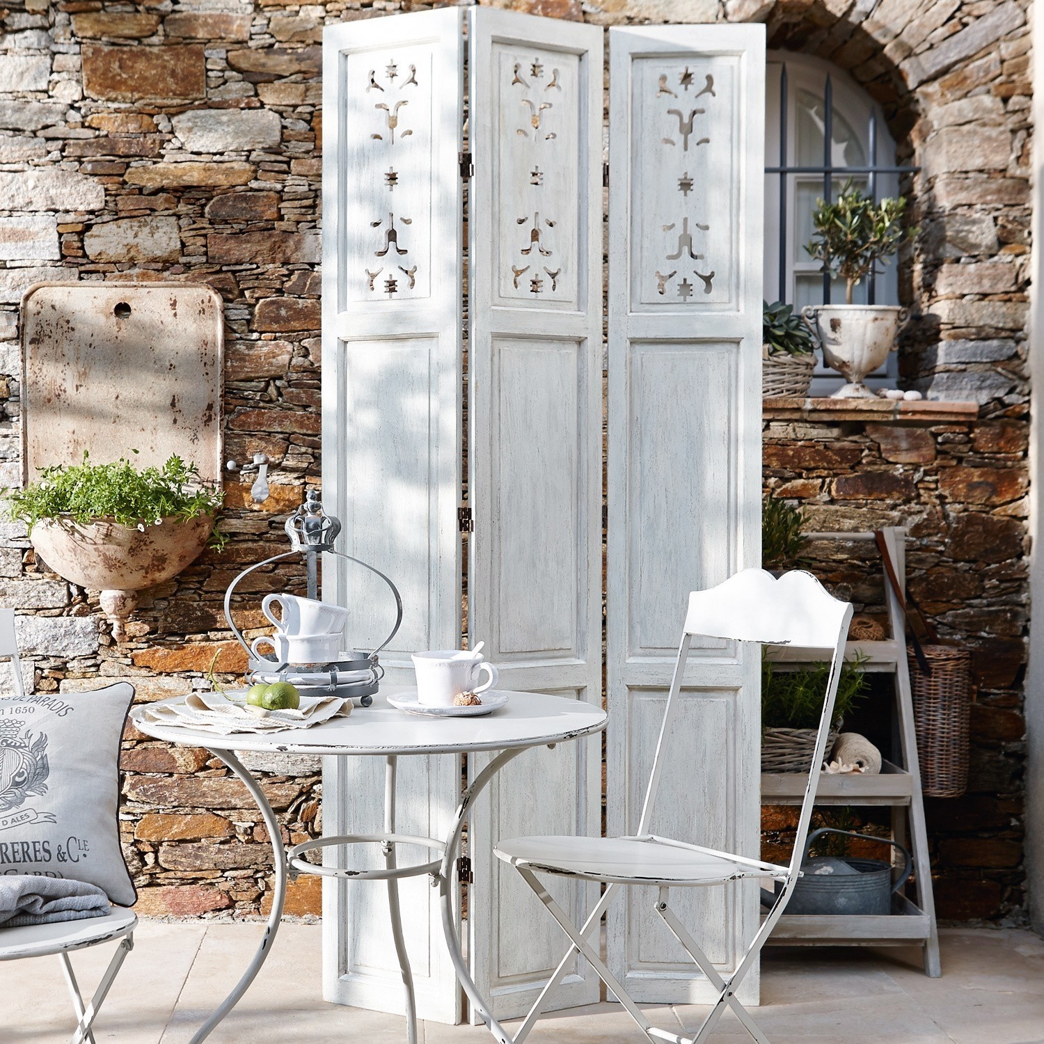 Weißer Metalltisch und Stuhl im Vintage-Stil auf Terrasse mit Steinmauer und Paravent