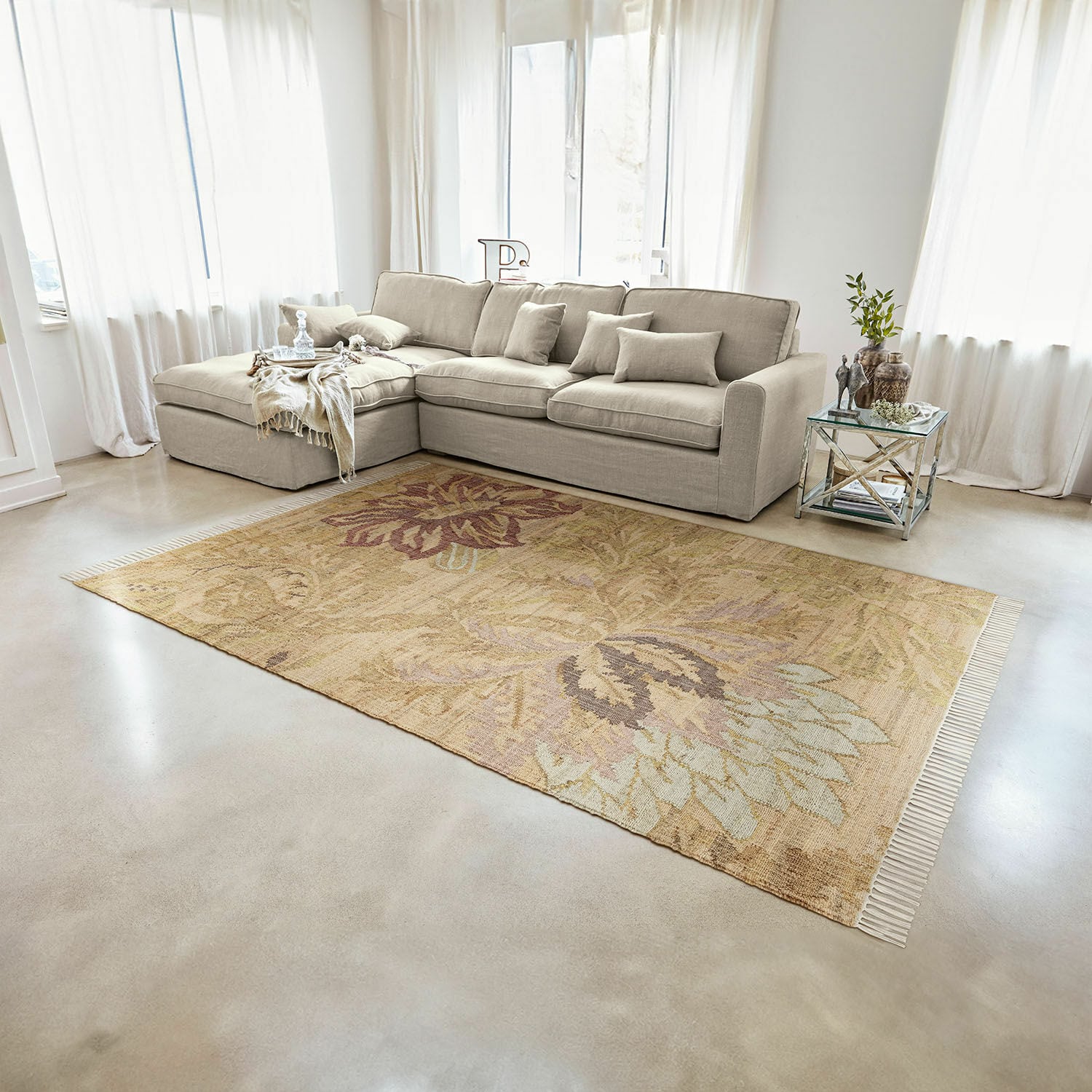 Teppich Willeque Beigefarbener Teppich mit floralem Muster aus Naturmaterial im hellen Wohnzimmer mit grauem Sofa