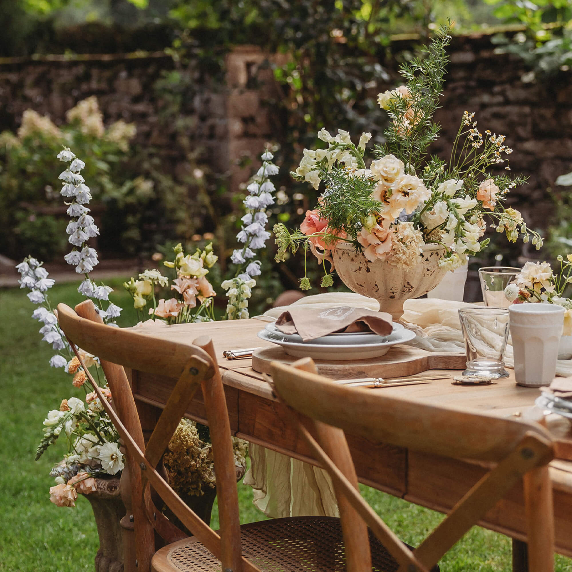 Holz-Gartentisch mit Blumenarrangement und natürlichen Stühlen auf grünem Rasen
