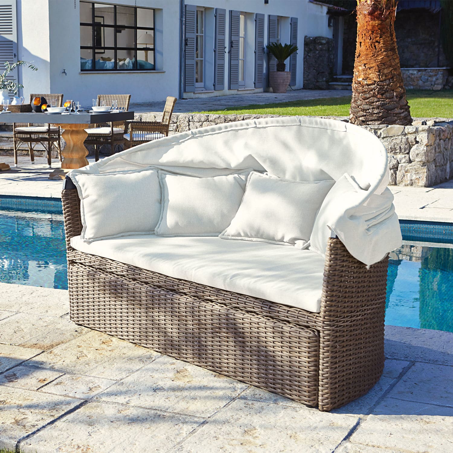 Gartensofa aus braunem Rattan mit cremefarbenen Kissen und Dach am Pool