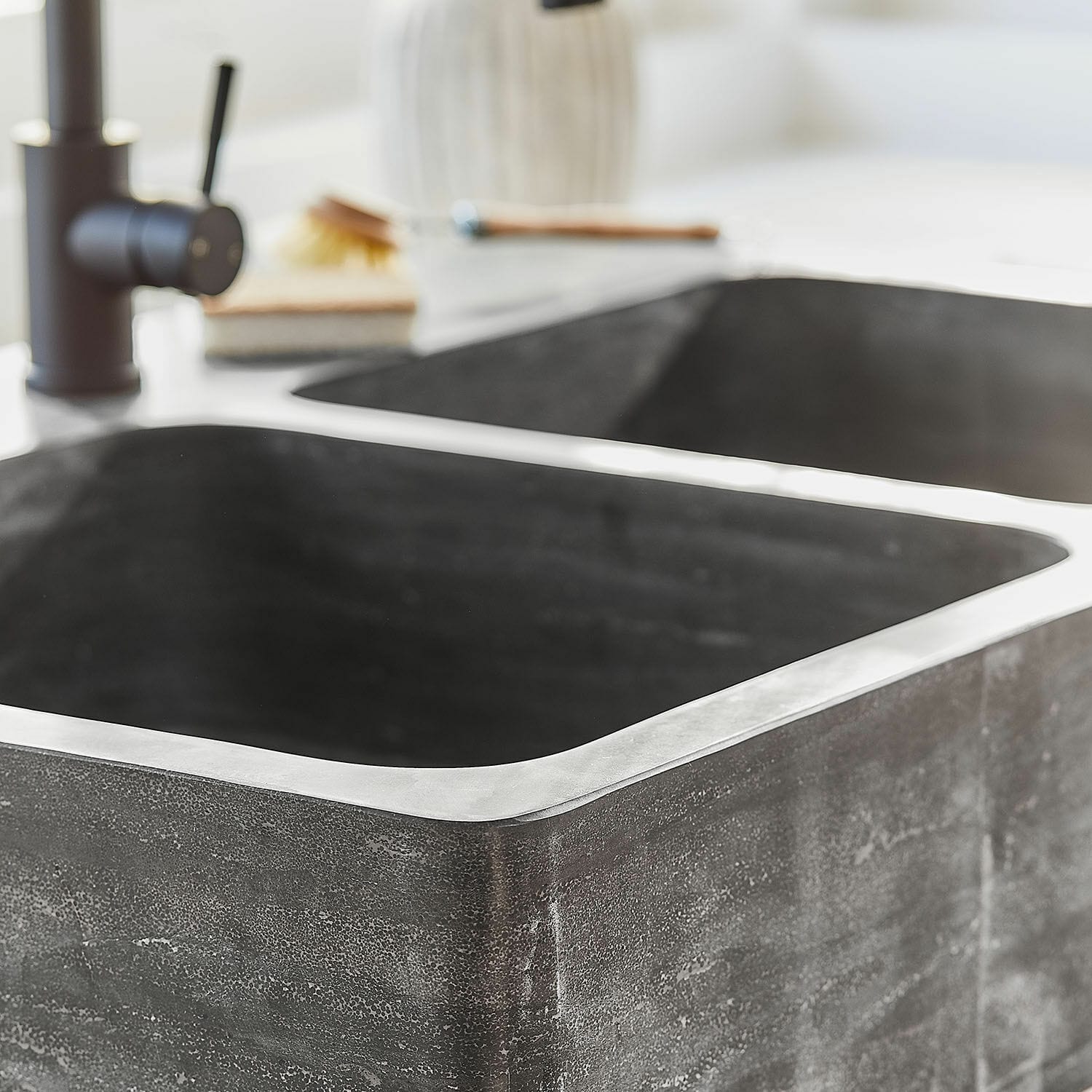 Moderner Küchenspülbecken aus schwarzem Stein mit Metallrand auf hellem Arbeitsplatte