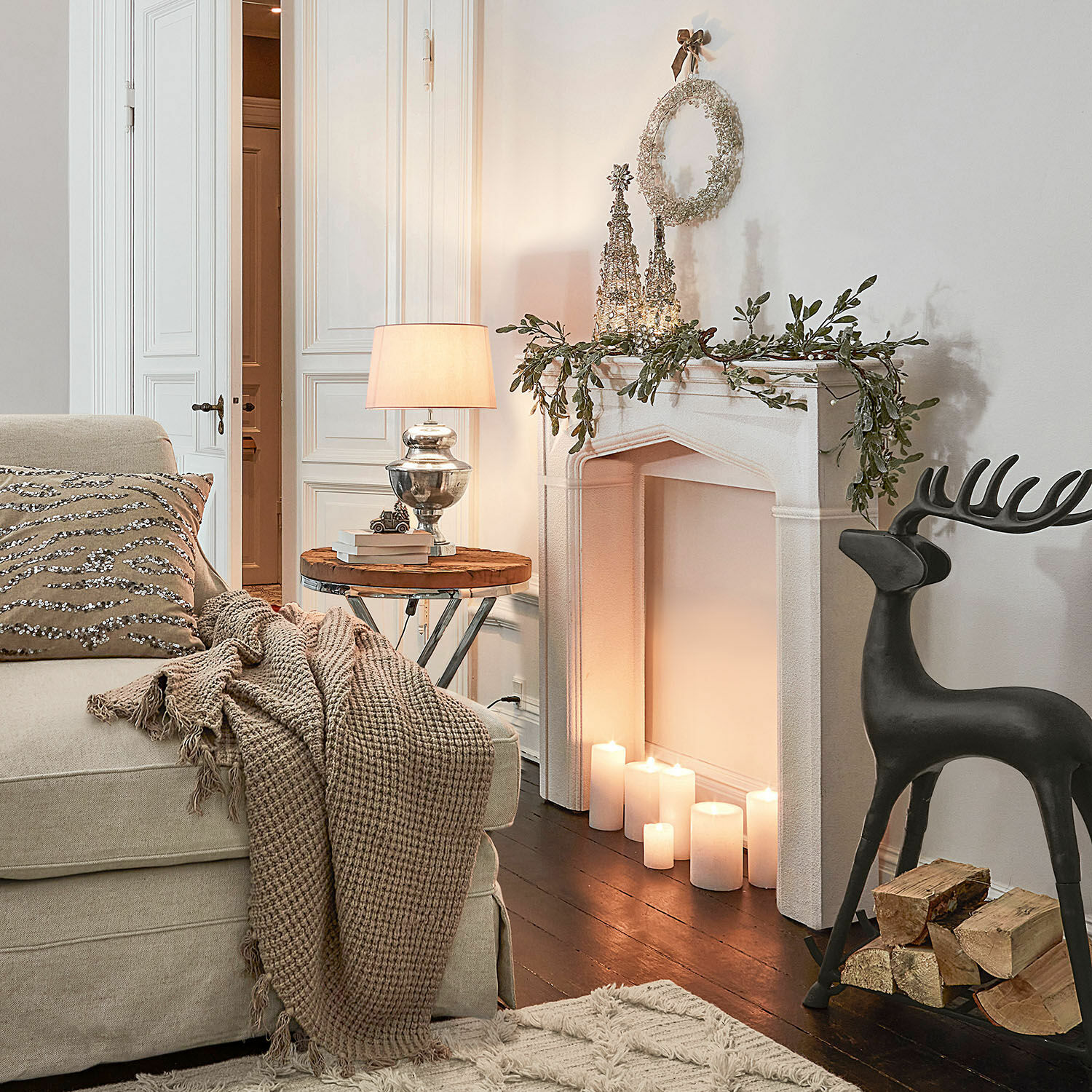 Gemütliches Wohnzimmer mit beigem Sofa, Decke, Kamin-Deko und brennenden Kerzen