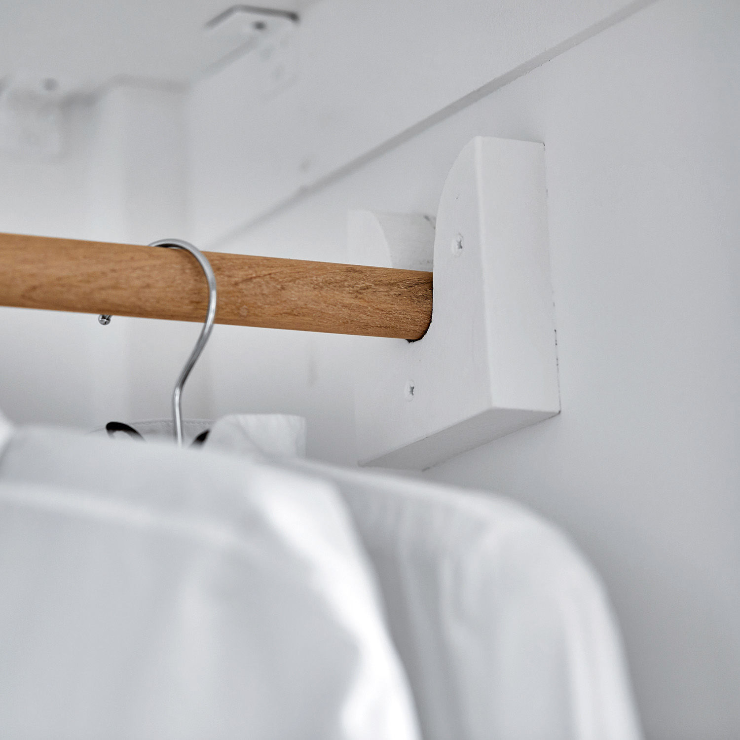 Holz-Kleiderstange mit weißer Wandhalterung in einem minimalistischen Schrank