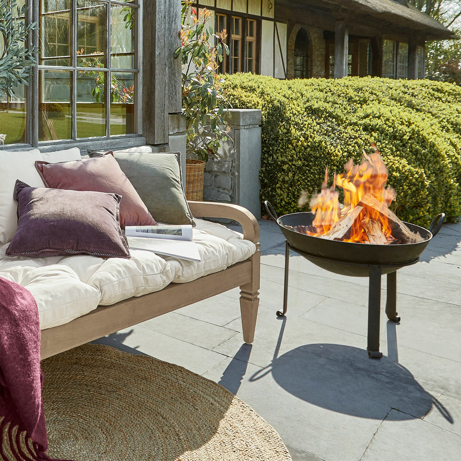 Garten mit schwarzem Metall-Feuerkorb und Holzbank mit pastellfarbenen Kissen für gemütliche Stunden