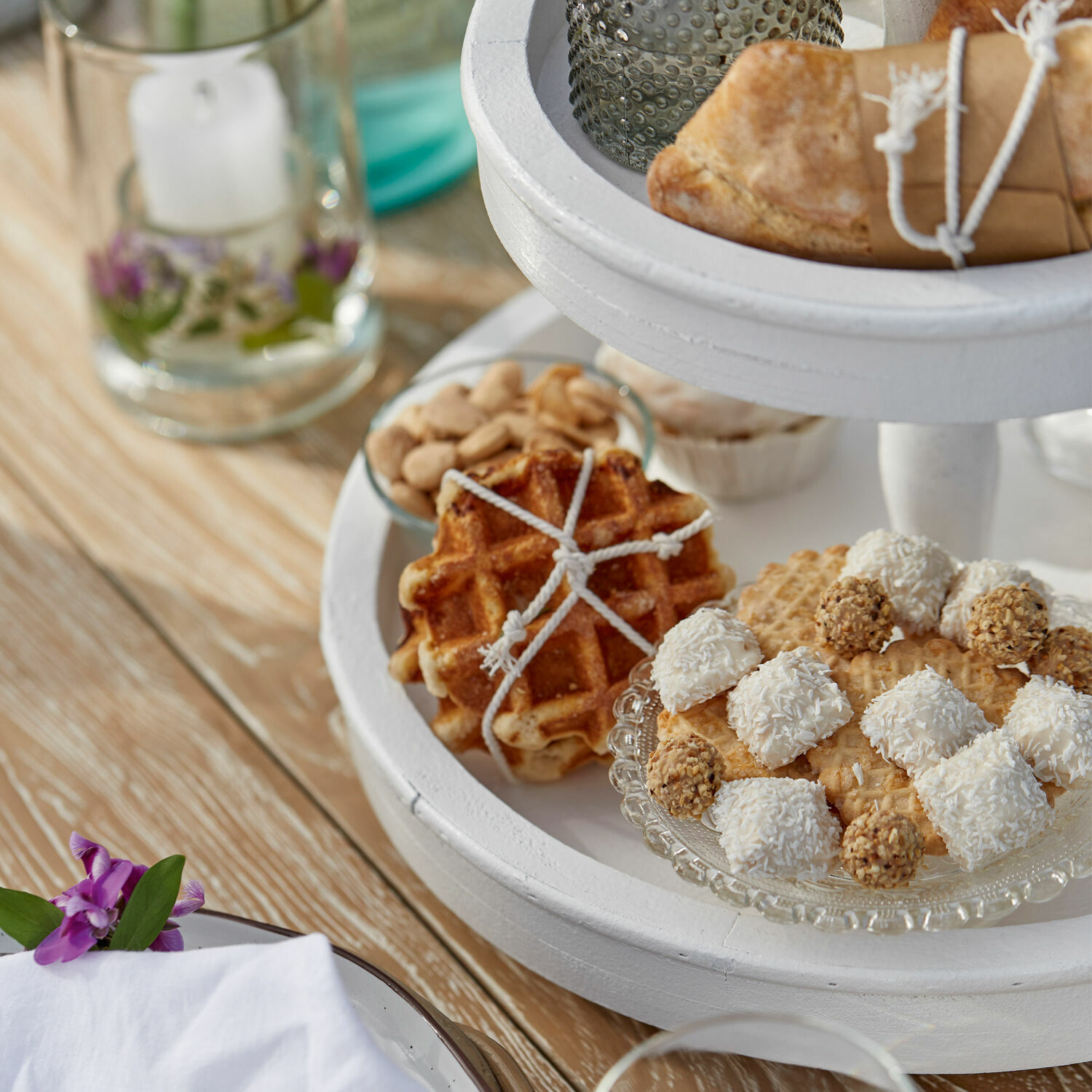 Weißer Holz-Etagere mit Waffeln und süßen Kugeln auf hellem Holztisch
