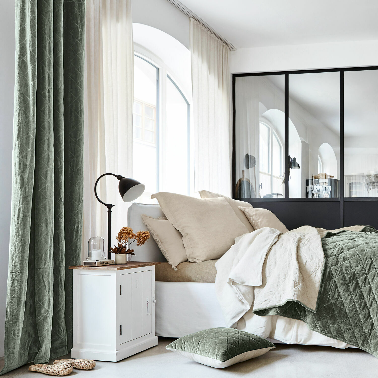 Gemütliches Schlafzimmer mit grünem Steppdecke und Kissen sowie weißem Nachttisch mit Lampe