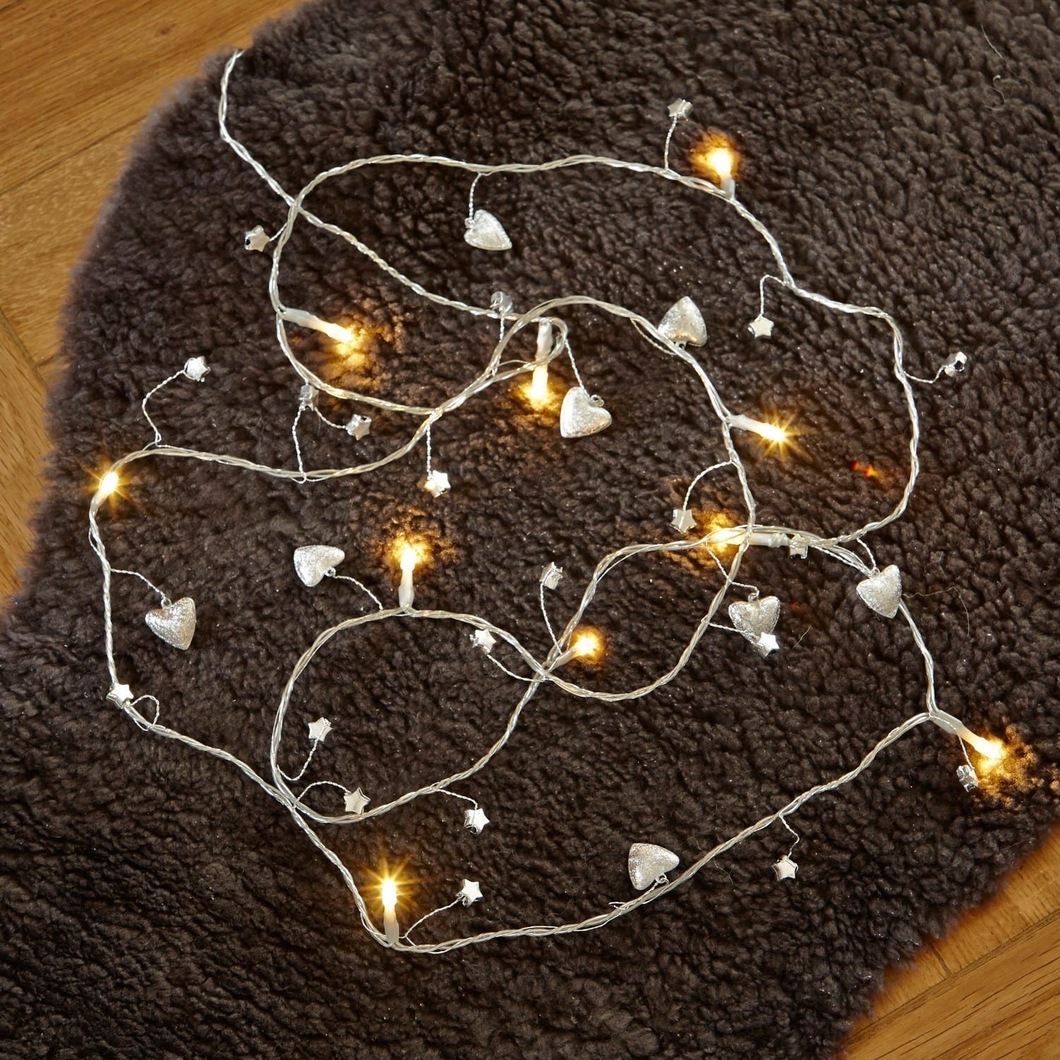 Dekorative Lichterkette mit silbernen Herzen und Sternen auf dunklem Teppich für Wohnraum