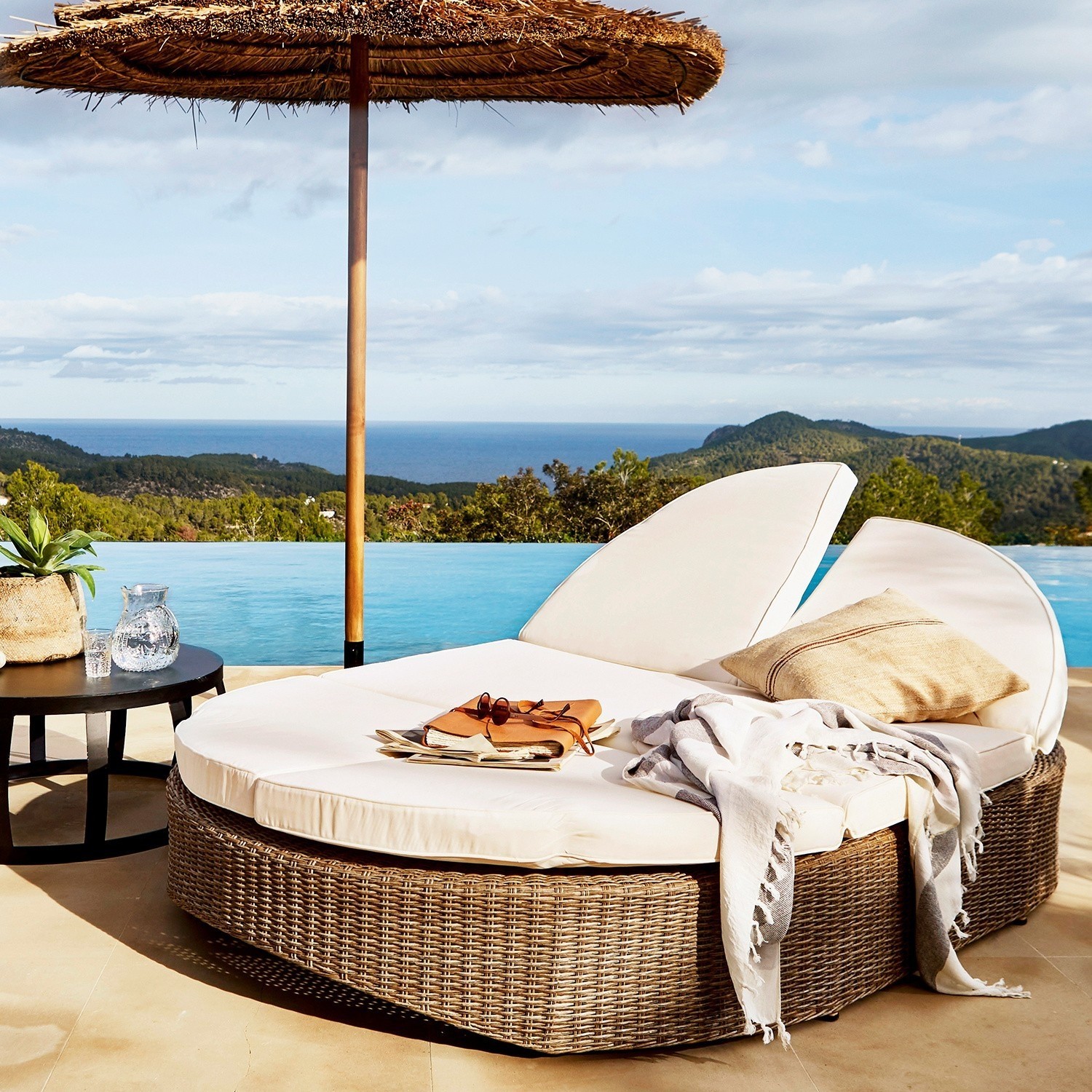 Runder Rattan-Liegestuhl mit cremefarbenen Polstern am Pool mit Meer- und Bergblick