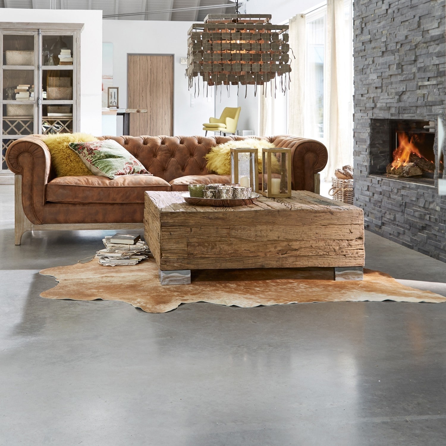 Wohnzimmer mit braunem Ledersofa, massivem Holztisch und Kamin vor hellen Wänden