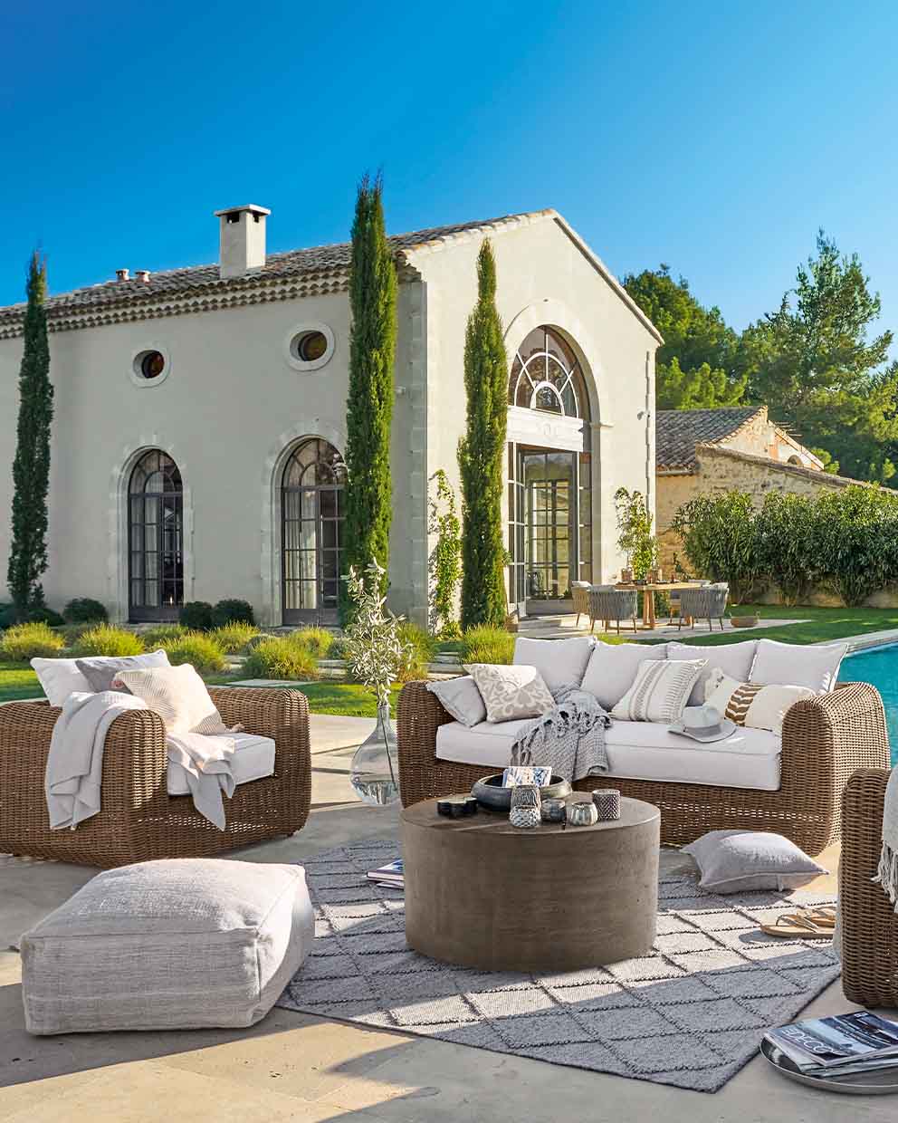 Braunes Rattan-Gartenmöbel-Set mit hellen Kissen auf Terrasse neben Pool im sonnigen Garten