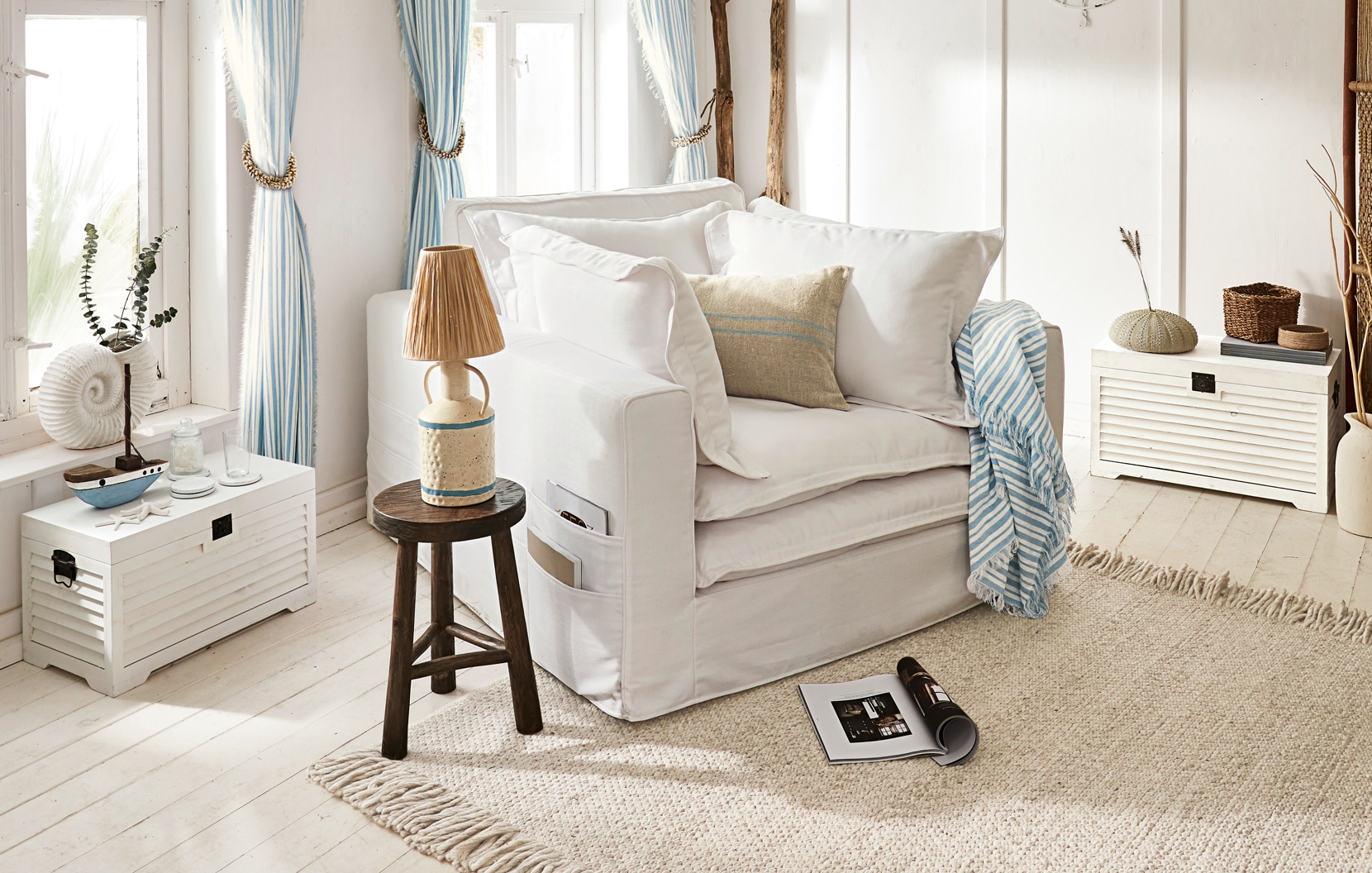 Gemütlicher weißer Sessel mit Kissen und blau-weiß gestreiftem Plaid in hellem, maritimem Wohnzimmer
