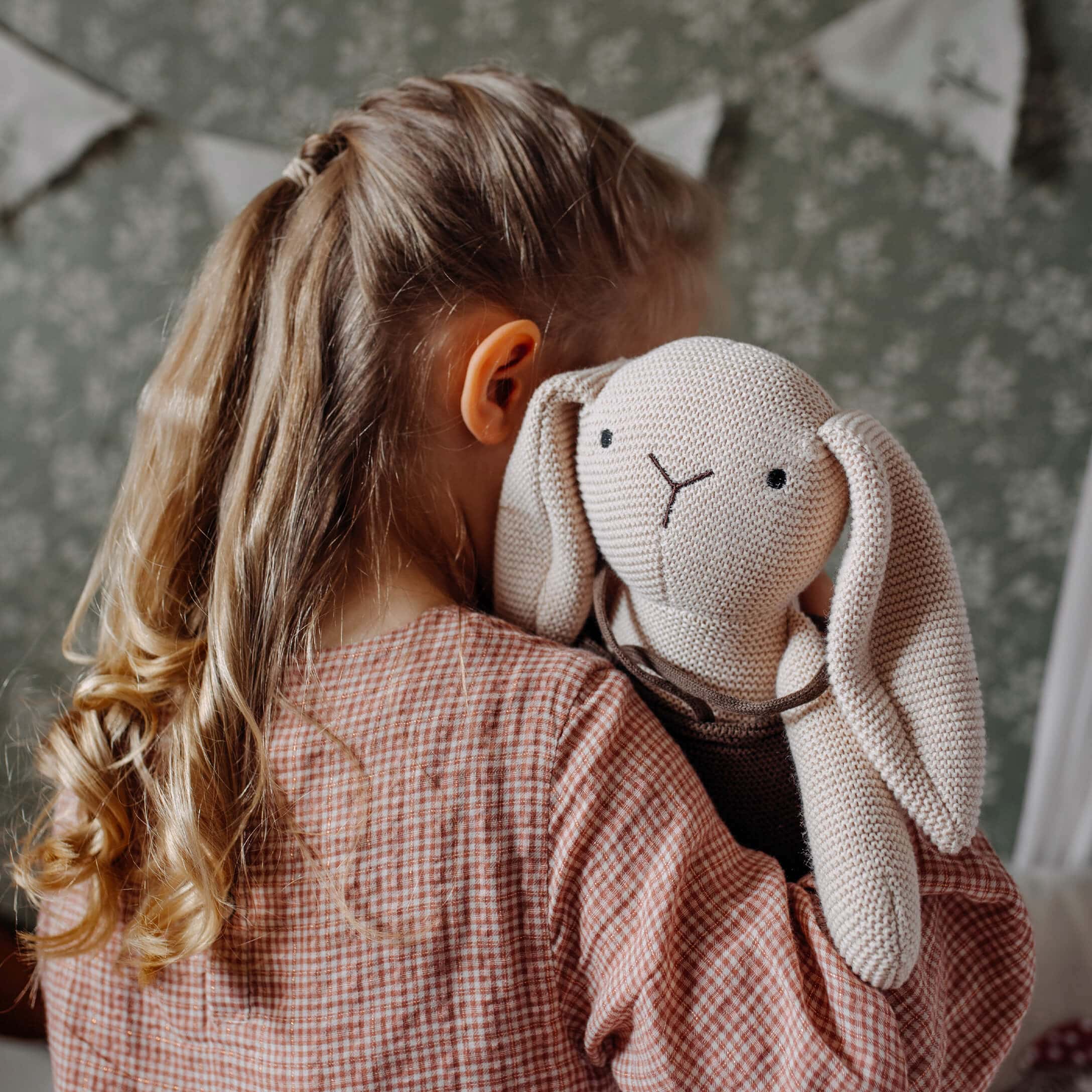 Mädchen umarmt beigen gestrickten Kuschelhasen im Kinderzimmer