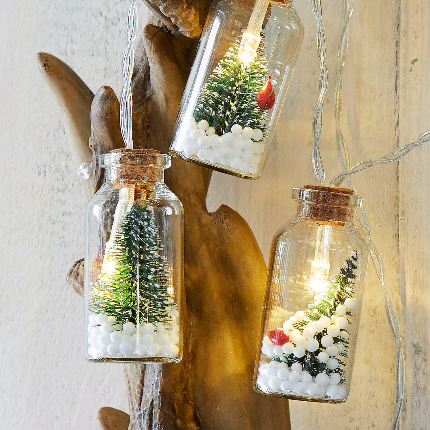 Lichterkette mit kleinen Tannenbäumen und weißen Kugeln in Glasflaschen, weihnachtliche Dekoration
