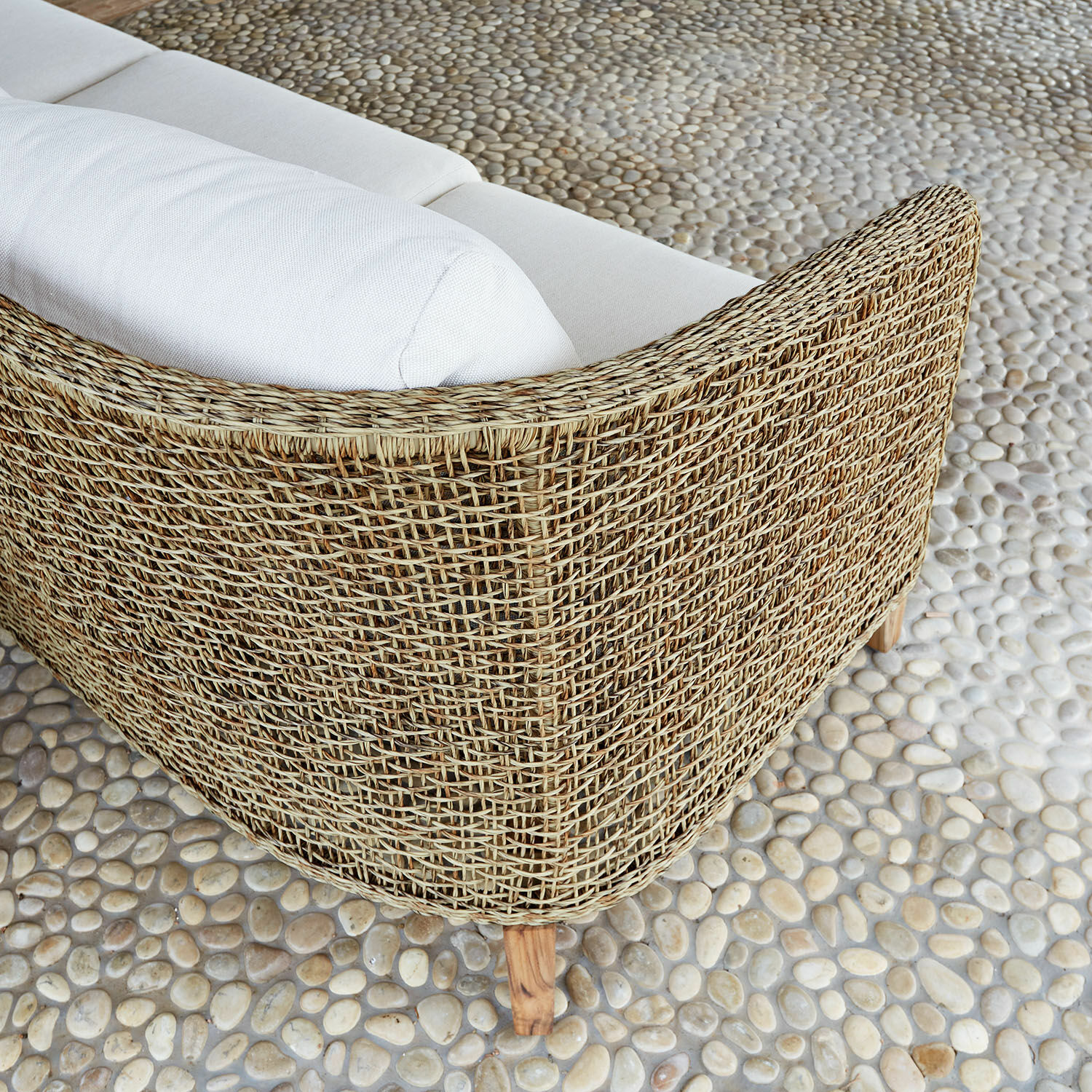 Sofa aus geflochtenem Rattan in Naturfarbe mit weißen Kissen auf Steinboden