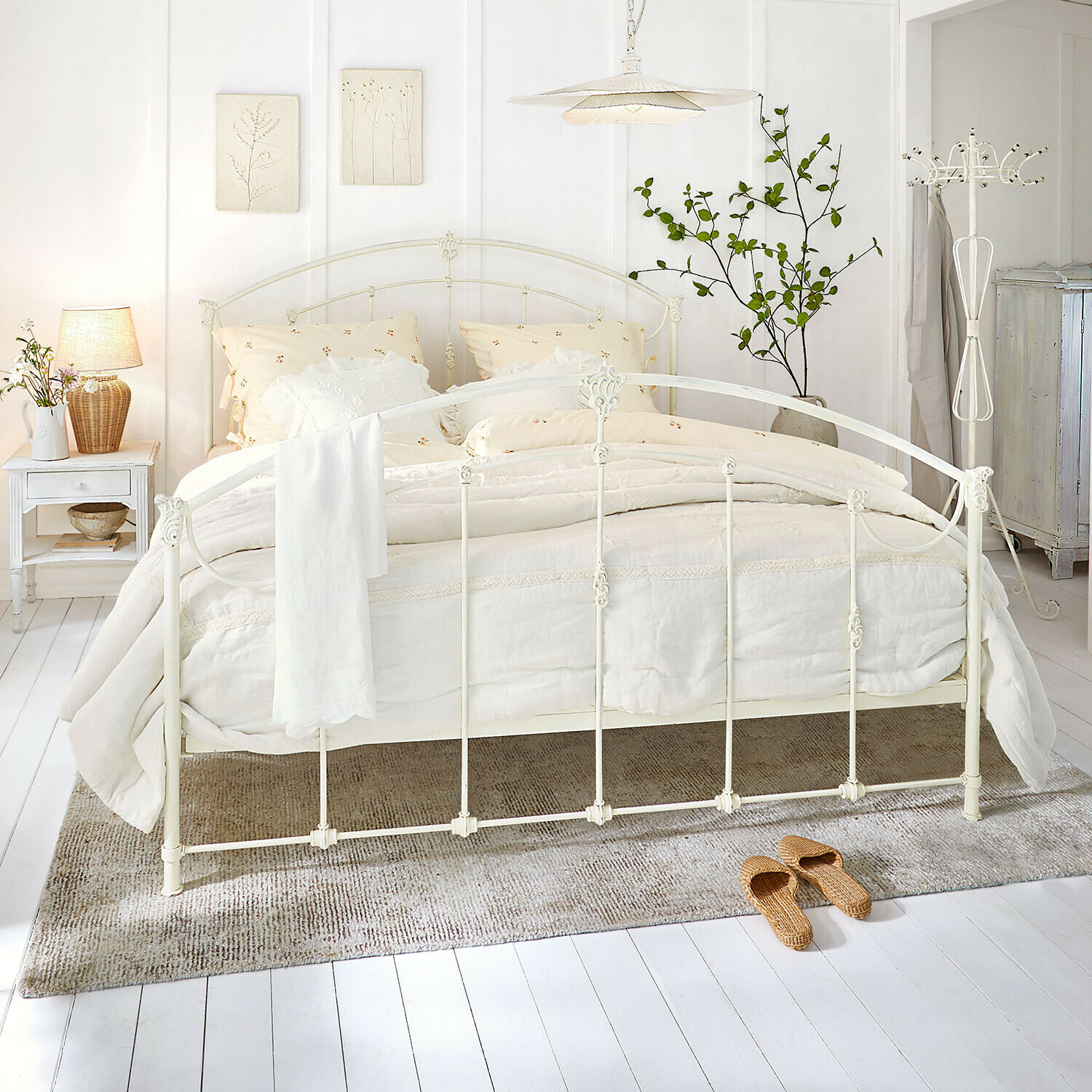 Bett Canefield Weißes Metallbett mit cremefarbener Bettwäsche und Naturteppich in hellem Schlafzimmer