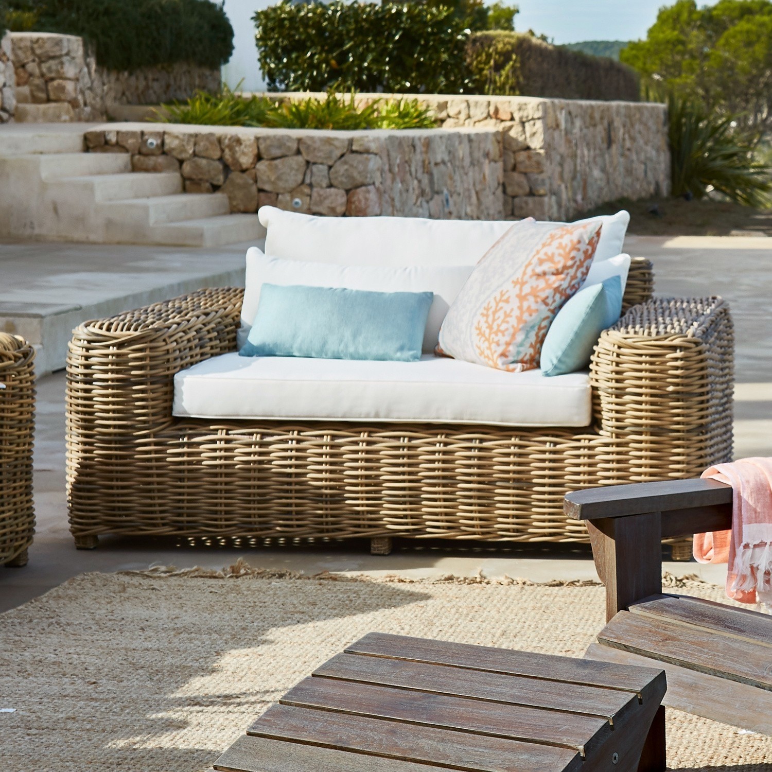 Rattansofa mit weißen Kissen und bunten Dekokissen auf Terrasse im Außenbereich