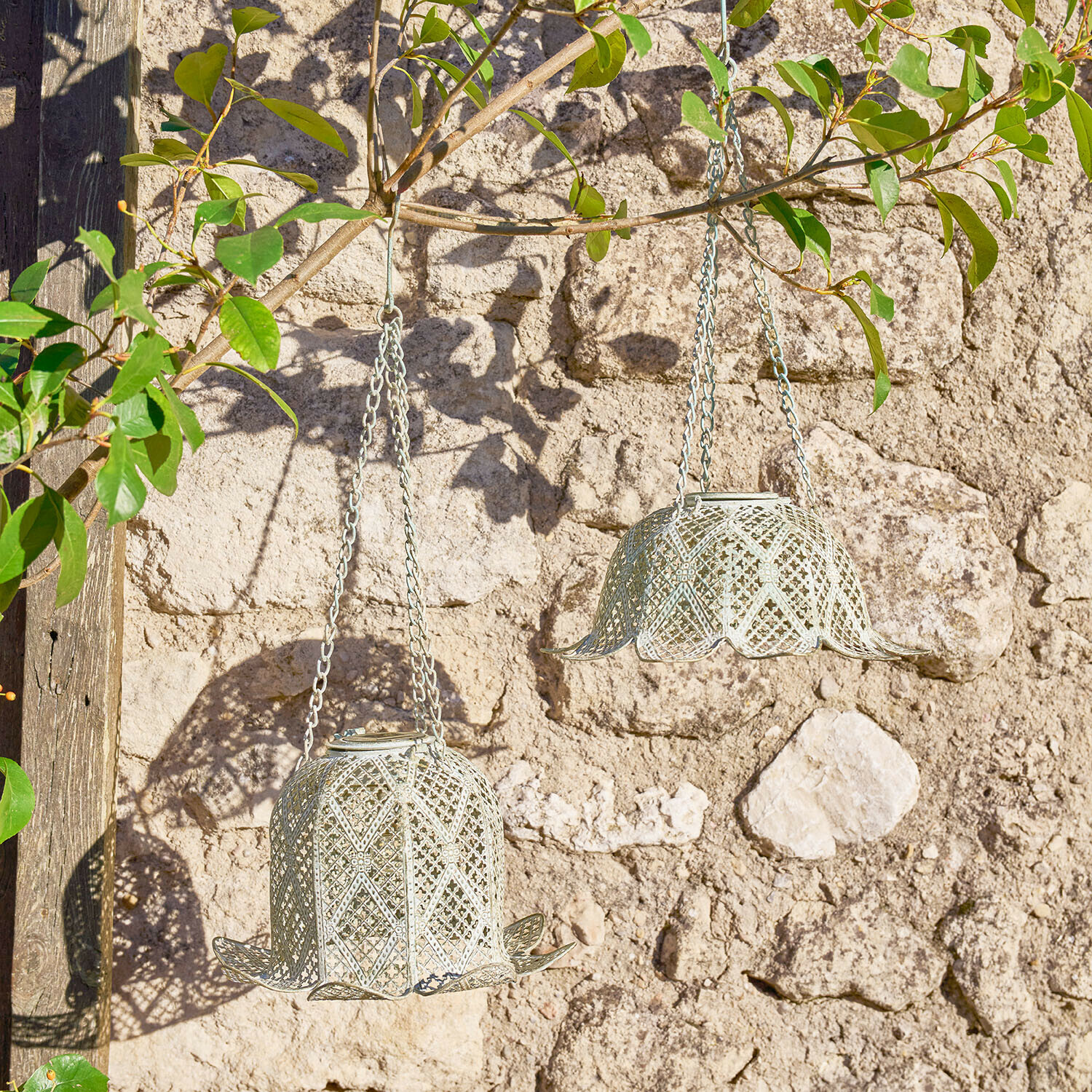 Zwei hängende Metalllaternen in Glockenform in Hellgrau vor einer Steinmauer