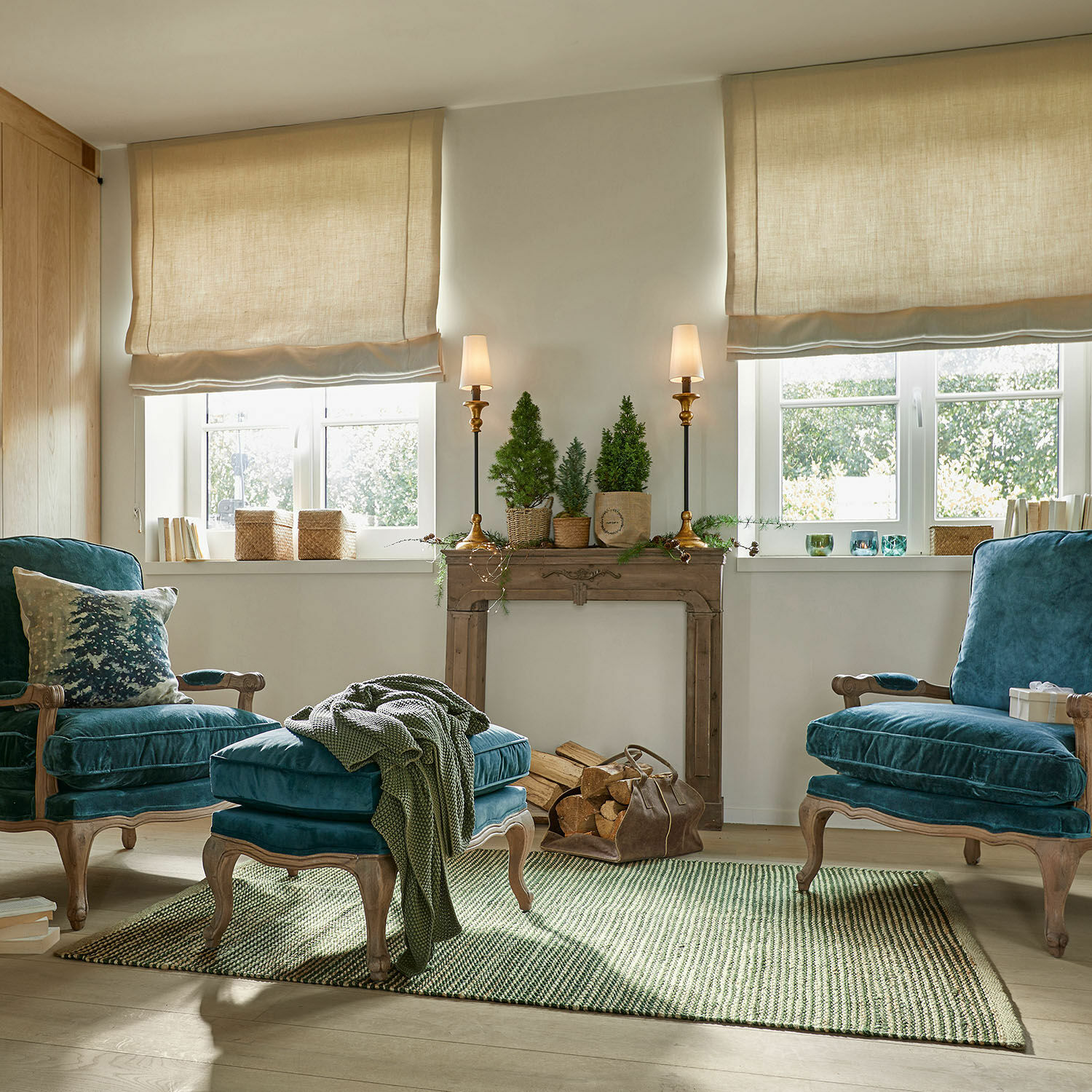 Gemütliches Wohnzimmer mit blauen Samtsesseln und grünem Teppich, Weihnachtsdeko und Kaminholz