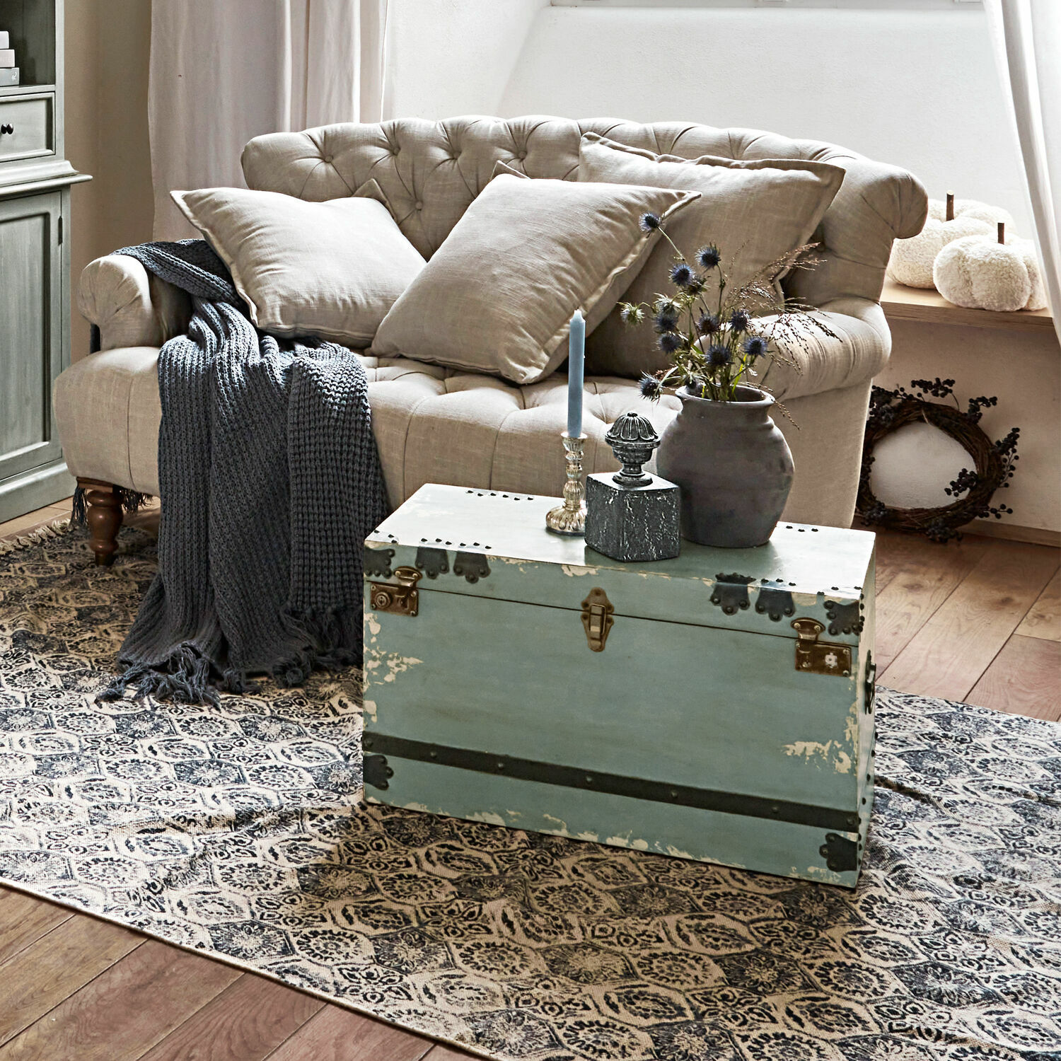 Beige gesteppte Sofa mit Leinenkissen und blauem Strickplaid auf gemustertem Teppich im Wohnzimmer