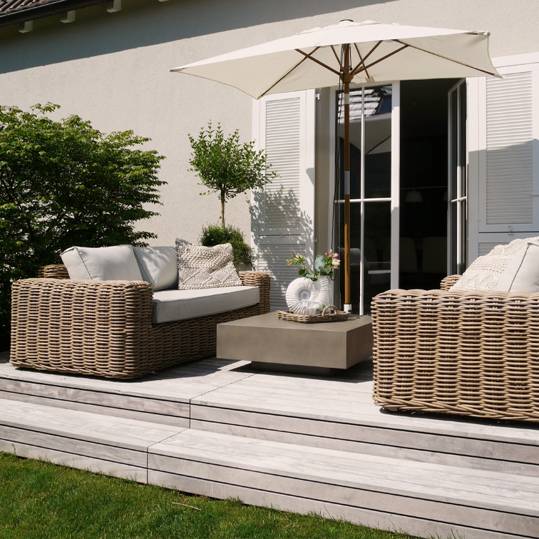 Moderner Gartenmöbel-Set aus beigem Rattan mit Sonnenschirm und Kissen auf hellem Holzdeck