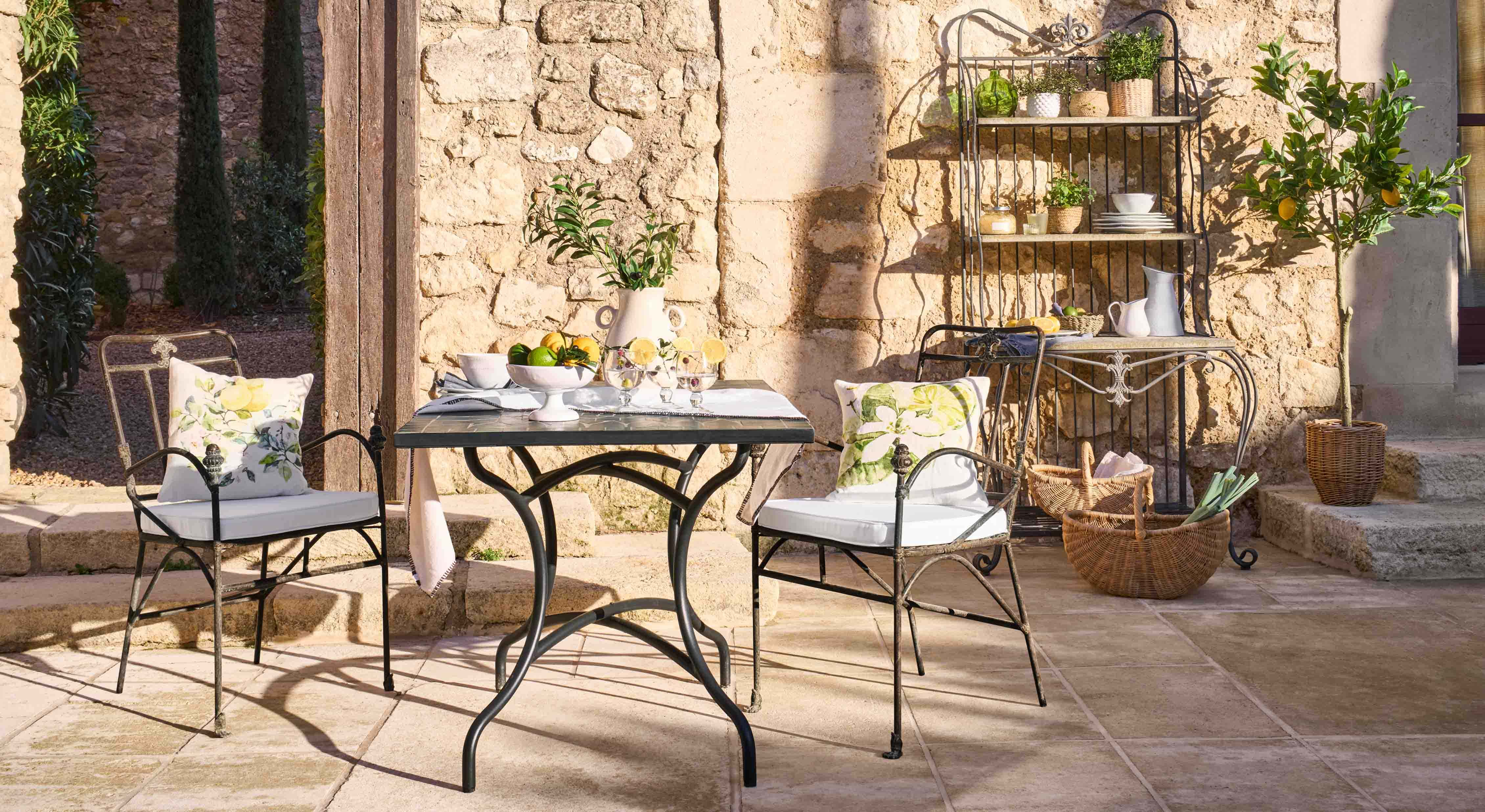 Metalltisch und Stühle mit floral gemusterten Kissen auf steinerner Terrasse mit Gartendekor