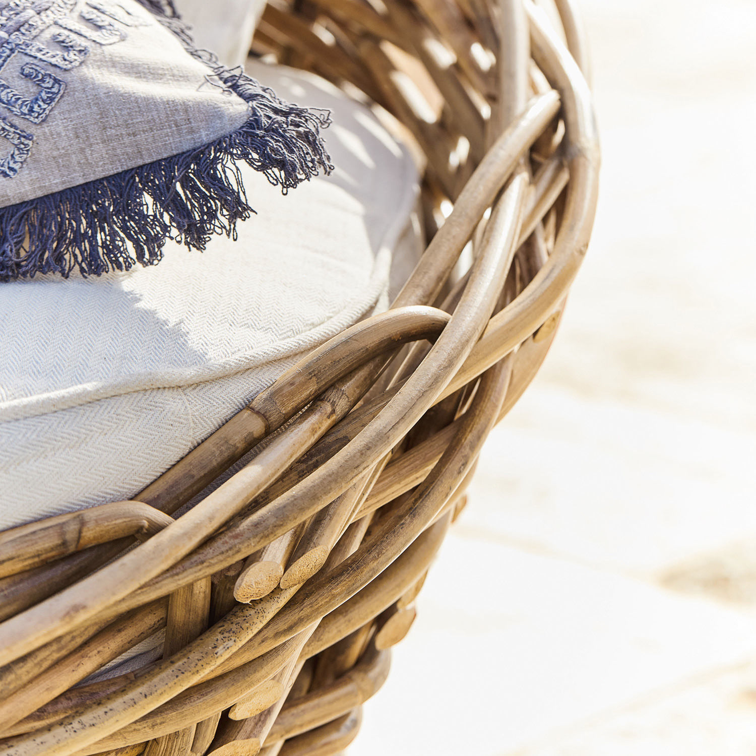 Natürlicher Rattansessel mit hellem Kissen und blauem Fransenplaid für Wohn- und Außenbereich