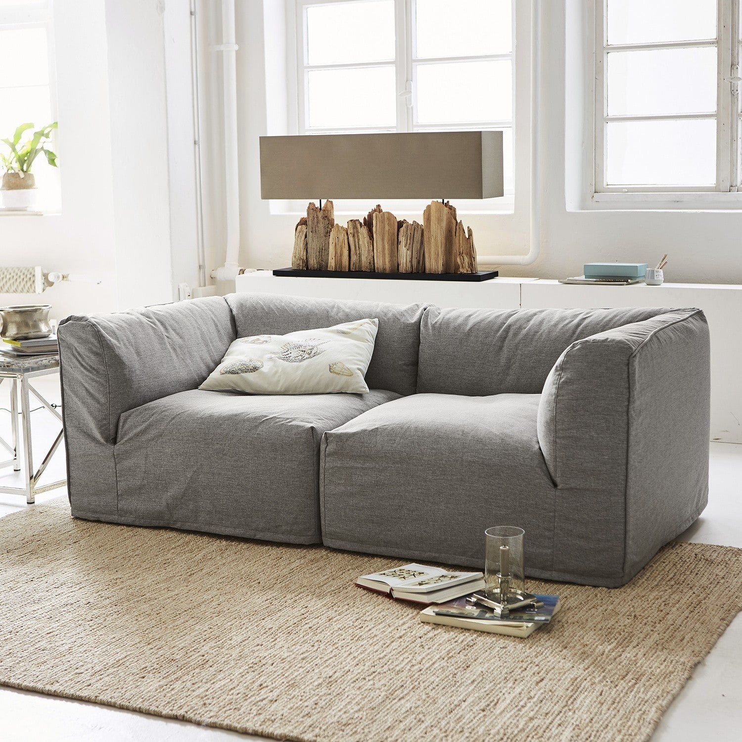 Graues Sofa aus Stoff auf beigem Teppich in hellem Wohnzimmer mit dekorativer Holzlampe