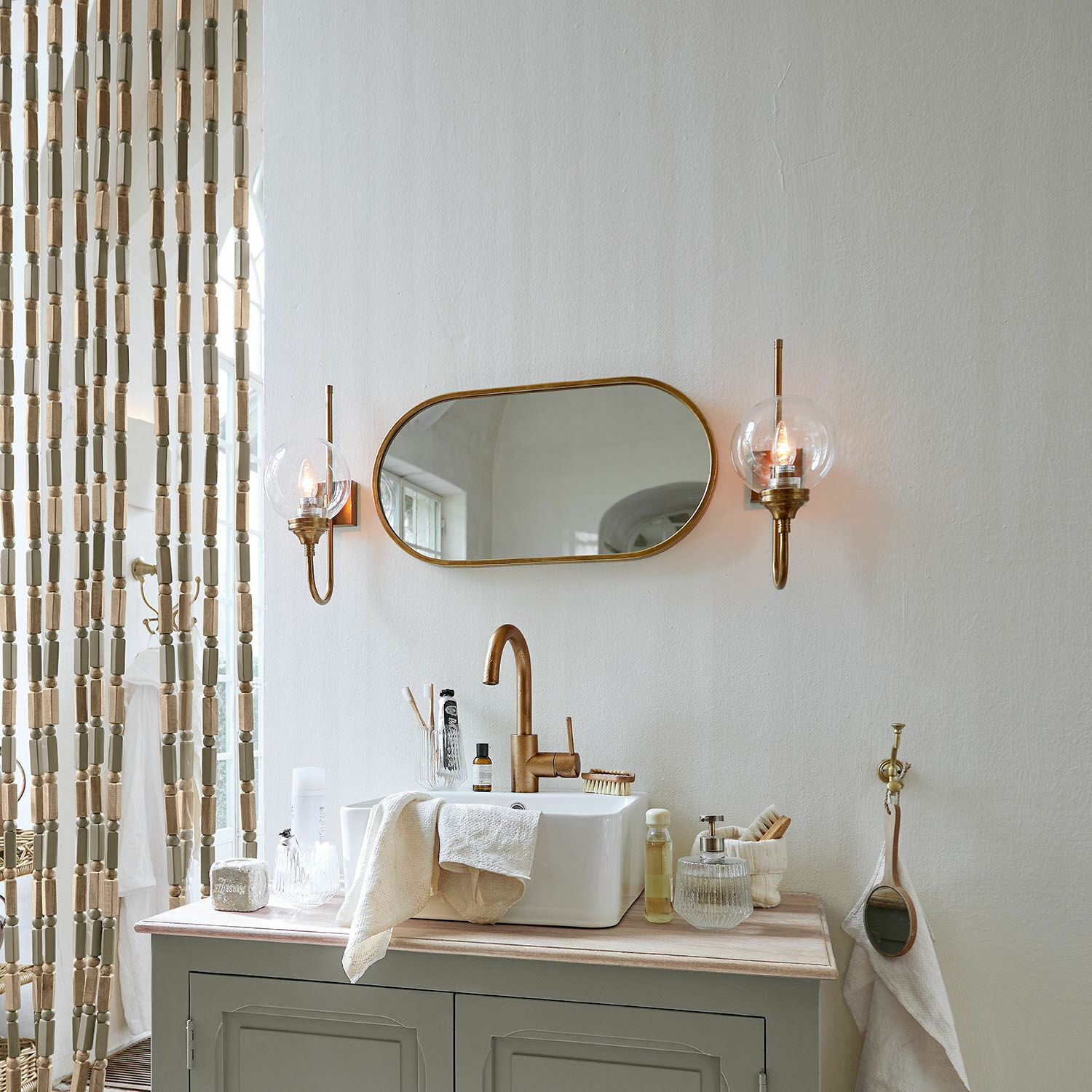 Badezimmer mit grünem Schrank, weißem Waschbecken, messingfarbenem Spiegel und Wandlampen im Vintage-Stil