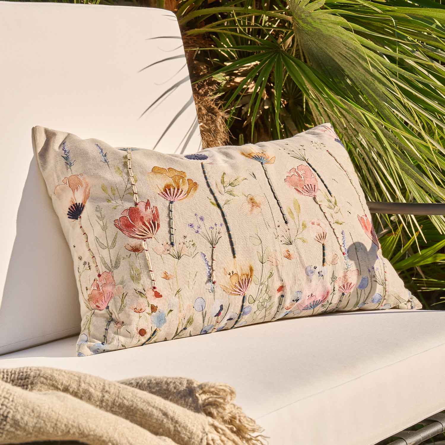 Beiges Dekokissen mit besticktem Blumenmuster auf hellem Stoff, ideal für Wohnzimmer und Garten