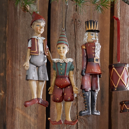 Drei hängende Holz-Weihnachtsfiguren in Rot und Grün vor rustikaler Holzwand