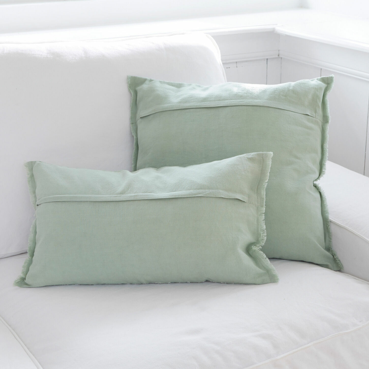 Set aus zwei hellgrünen Leinen-Dekokissen auf weißem Sofa für Wohnzimmer