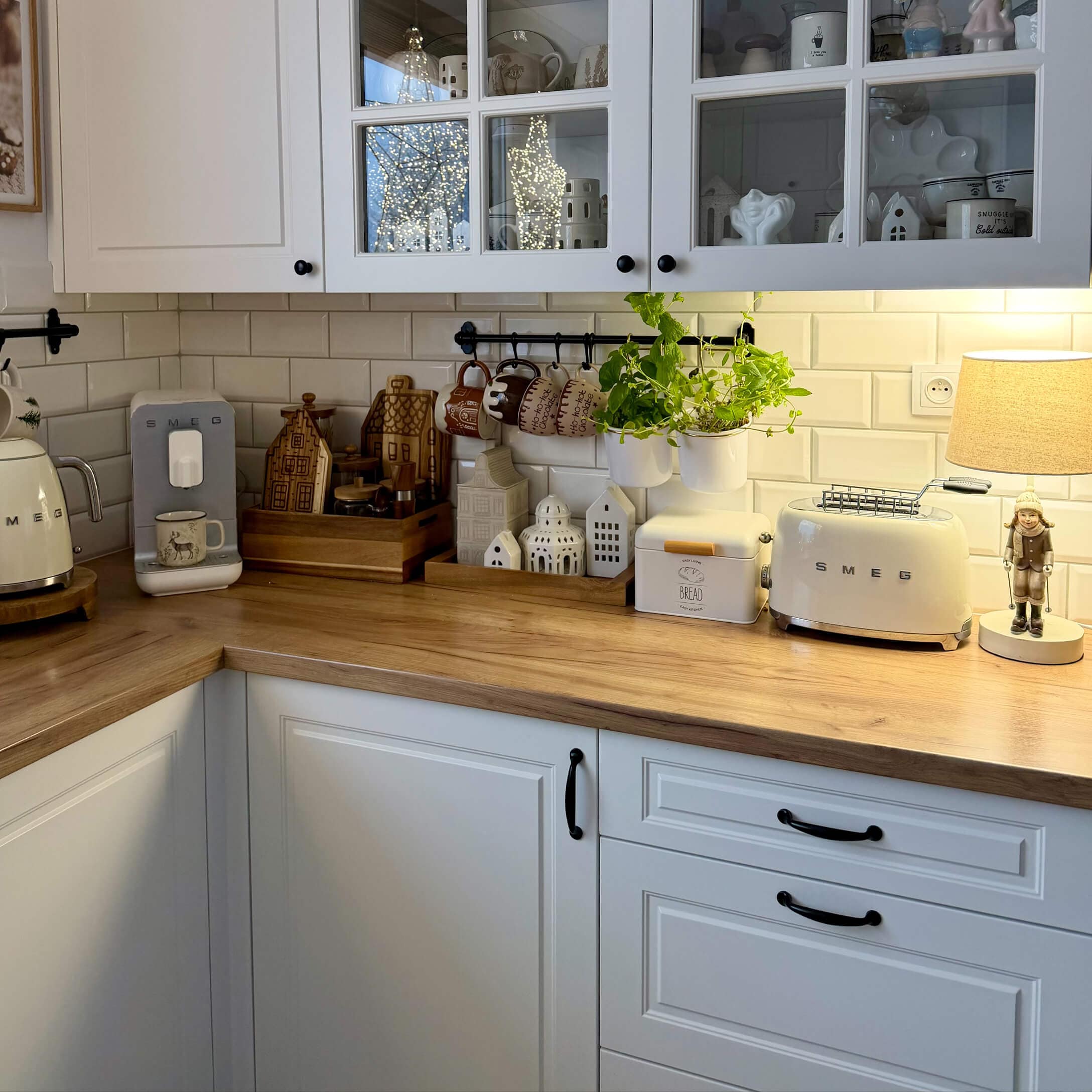 Küche mit weißen Schränken, Holzarbeitsplatte, cremefarbenen SMEG-Geräten und Dekorationen mit Pflanzen